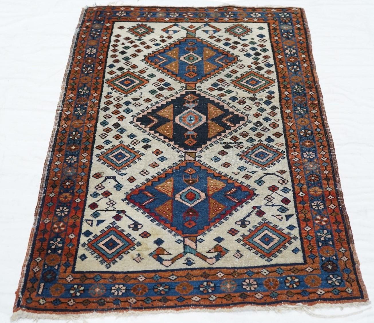 Vintage Persian Rug 2'6'' x 4'6''. The ecru field centres a pole medallion of three tab-fringed diamonds in medium blue and black, with red stylized leaf details. Smaller end suite nested diamonds and tertiary rosettes scattered about. Angular ram's