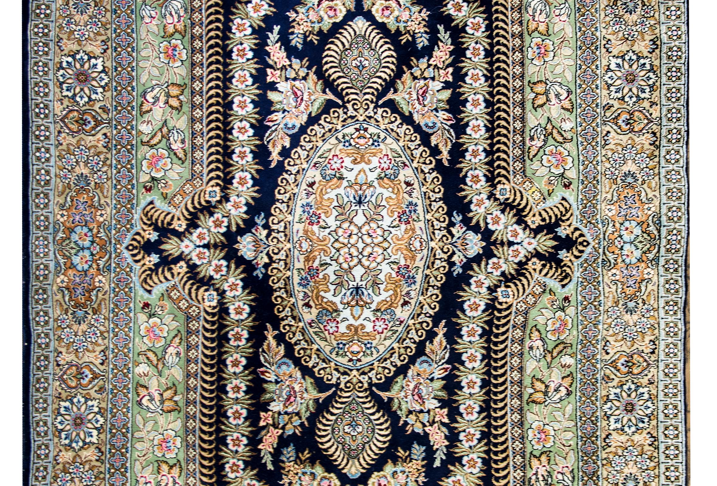 A lovely late 20th century Persian Rum rug with an intensely woven floral medallion with a lively energy, and surrounded by a complex border of wide and narrow floral patterned stripes.