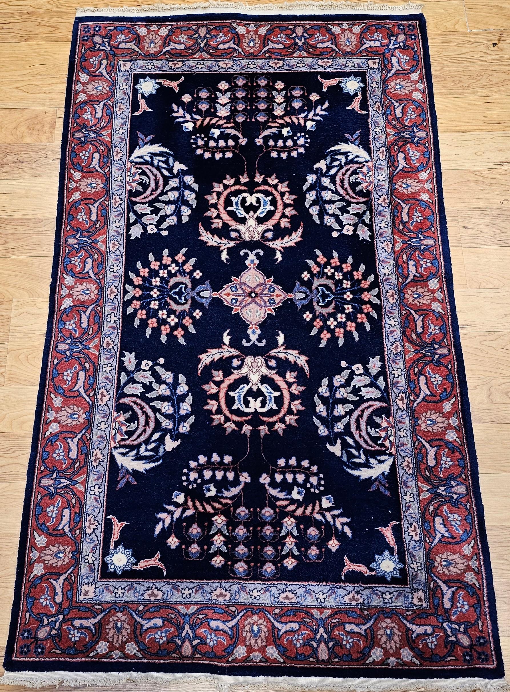 Vintage persischen Sarouk Bereich Teppich in einem allover floralen Muster circa das 3. Quartal des 1900er.  Der Sarouk-Teppich hat einen marineblauen Hintergrund mit großformatigen floralen Mustern in Blau, Gelb, Rot und Rosa.  Der Teppich hat eine