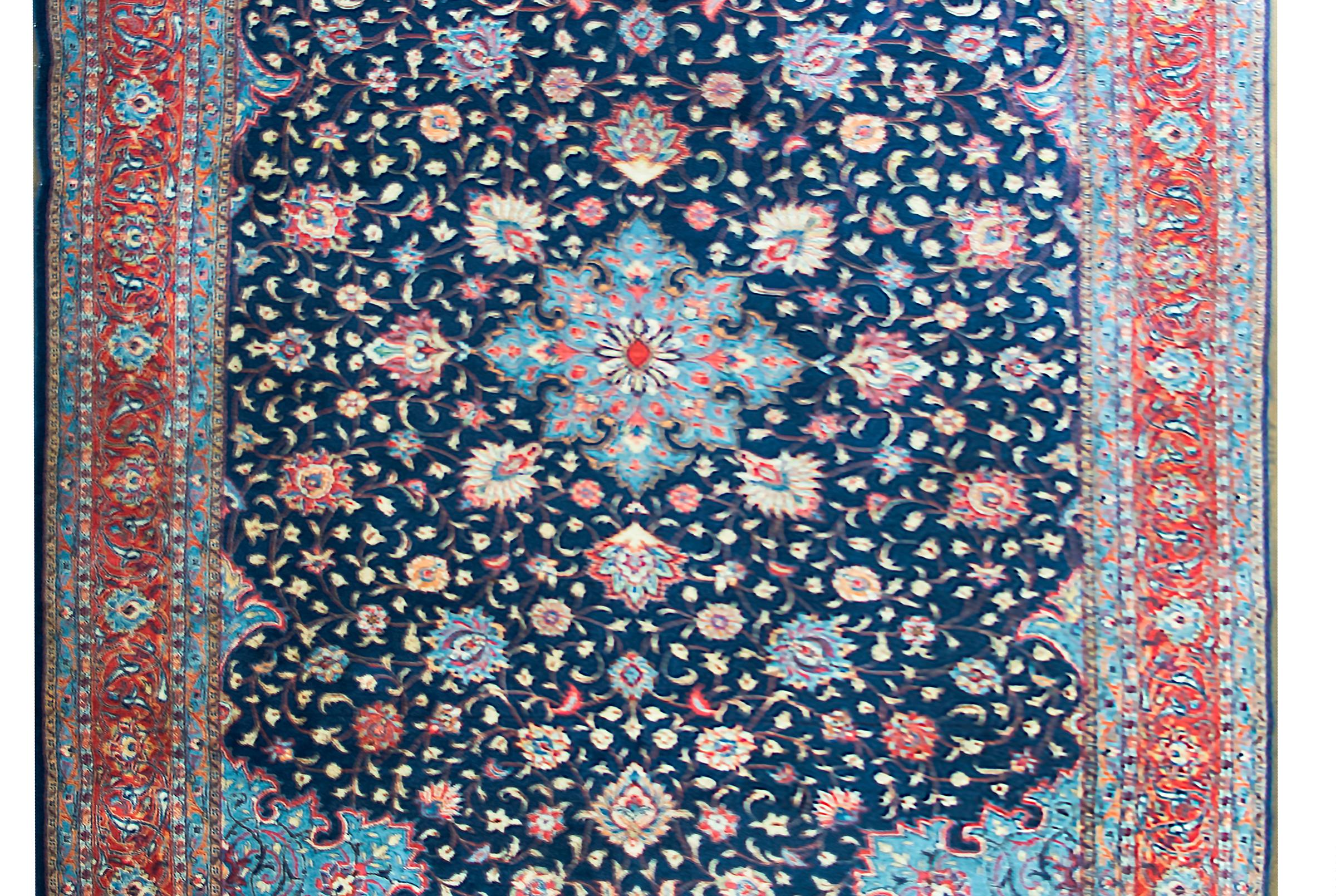 A beautiful mid-20th century Persian Sarouk rug with a central flower with trailing vines with more large flowers and leaves, surrounded by a complex border with a repeated floral and vine pattern, and all woven in light and dark indigo, crimson,