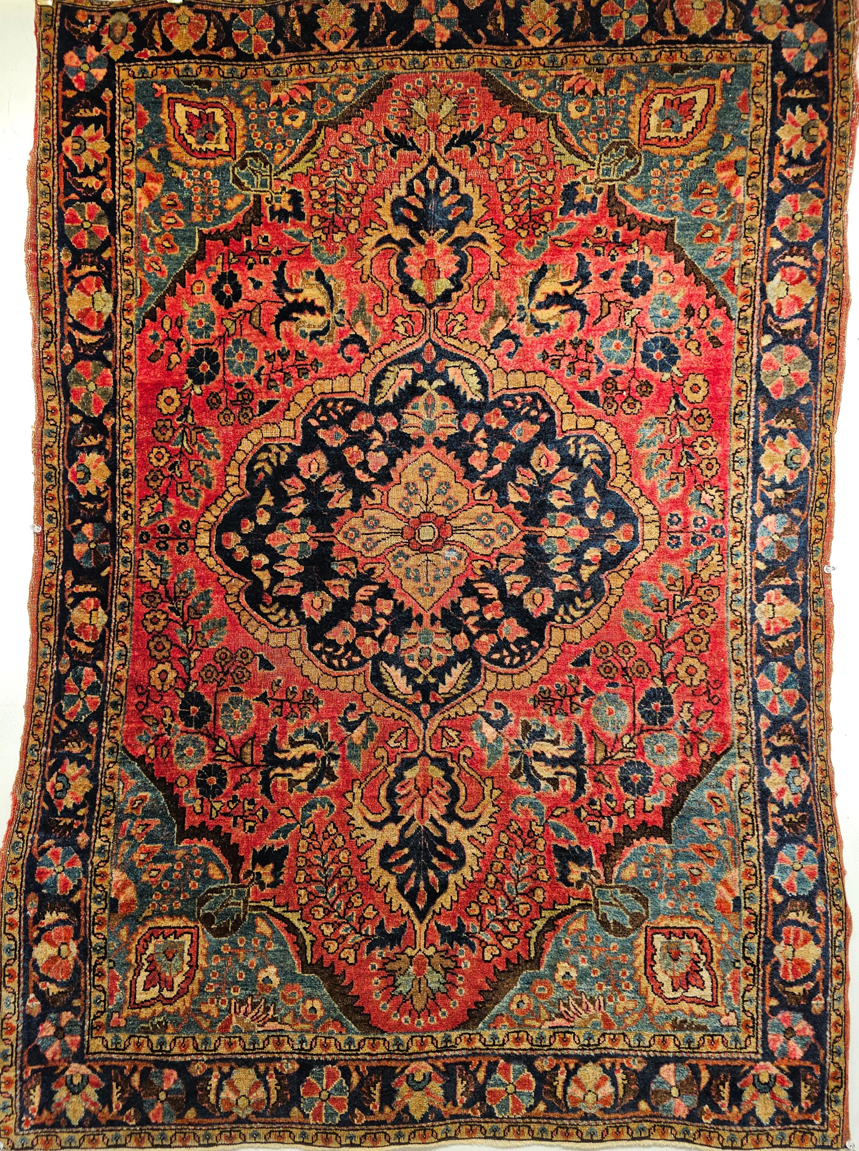 A wonderful small Sarouk area rug from the 1st quarter of the 1900s. The rug has a floral design set in a red color field with flowers and leaves in green, blue, red, yellow, and pink colors. The rug has a central medallion and its border in navy