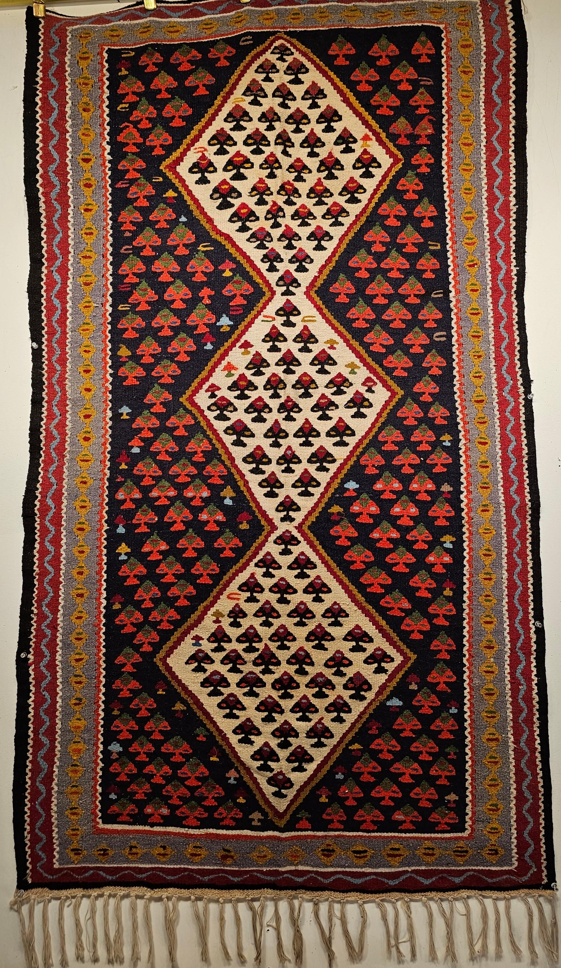 A beautiful vintage Persian Senneh kilim area rug from the Kurdish region of Western Persia. The Senneh Kilim has the repeated form of a small flower head in the center white 3 diamonds placed in a field of black color with the flowers in red.  
