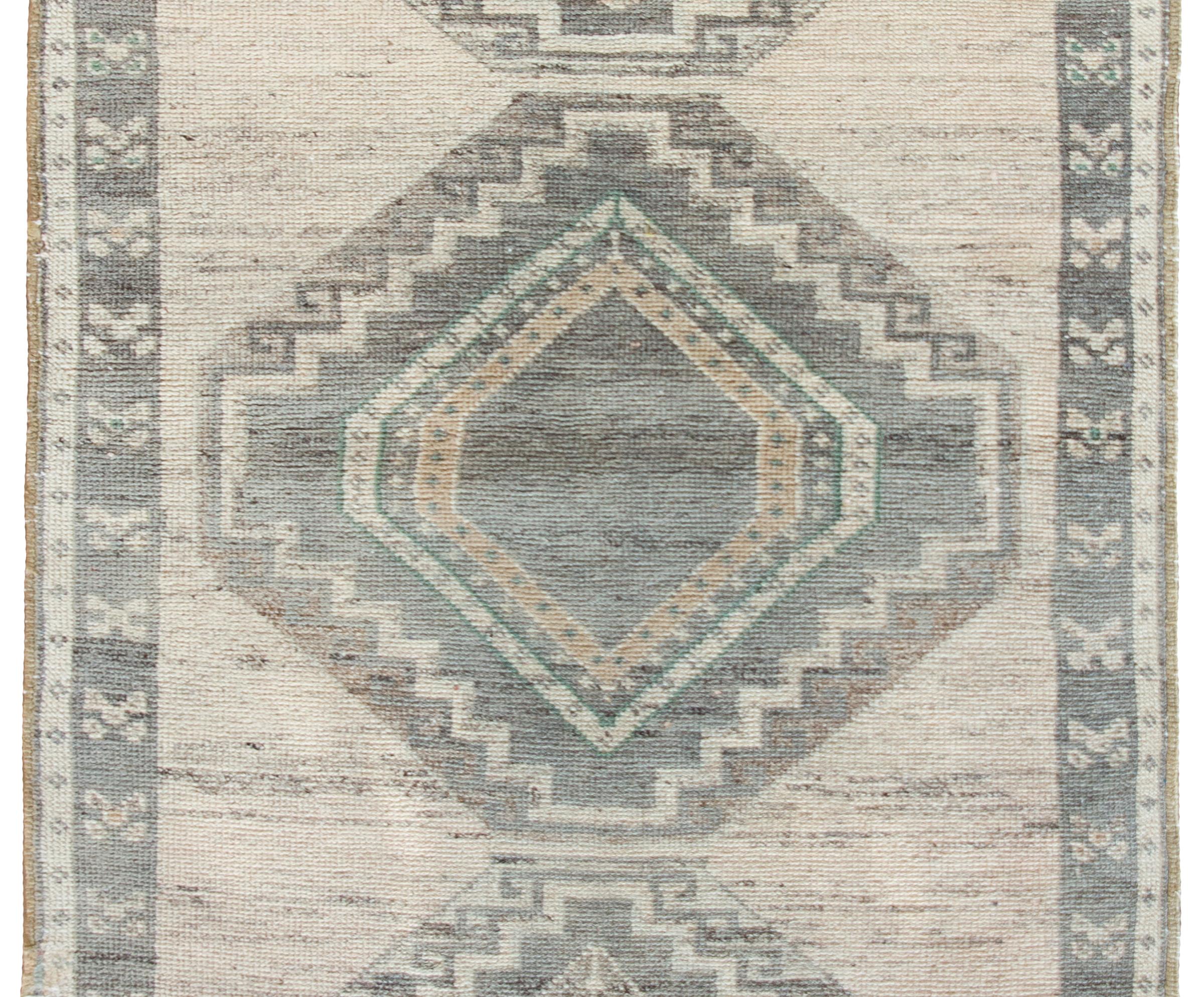 A vintage Persian Serab rug with three large geometric diamond medallions surrounded by a simple border with even more geometric stylized flowers, and all woven in simple grey, browns, and creams.  