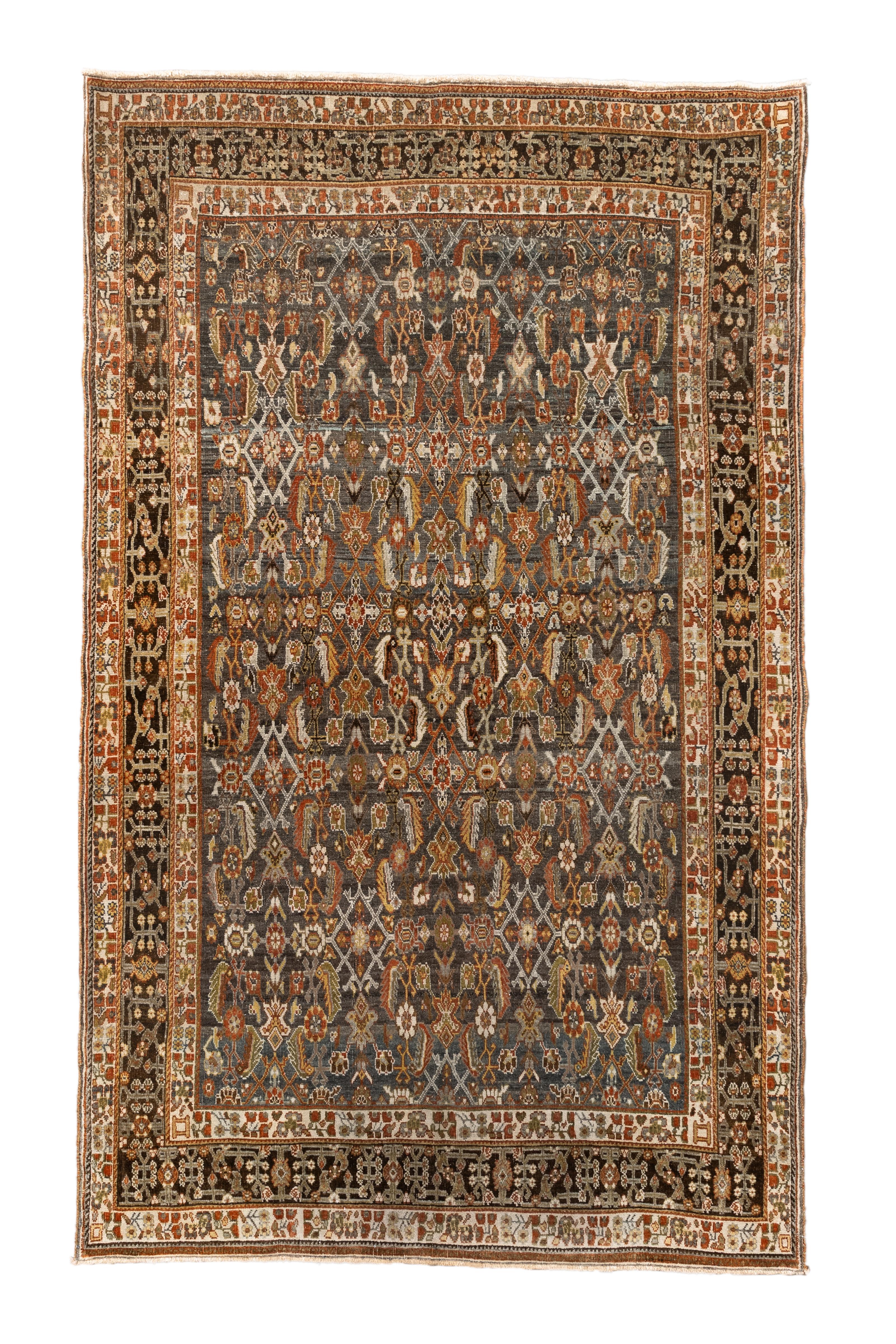  A stunning vintage Persian Shiraz rug featuring a densely patterned field of tribal motifs in a sophisticated palette of earthy browns, soft blues, muted rusts, and ivory. Measuring 4 feet 6 inches by 7 feet 4 inches, this handwoven wool rug