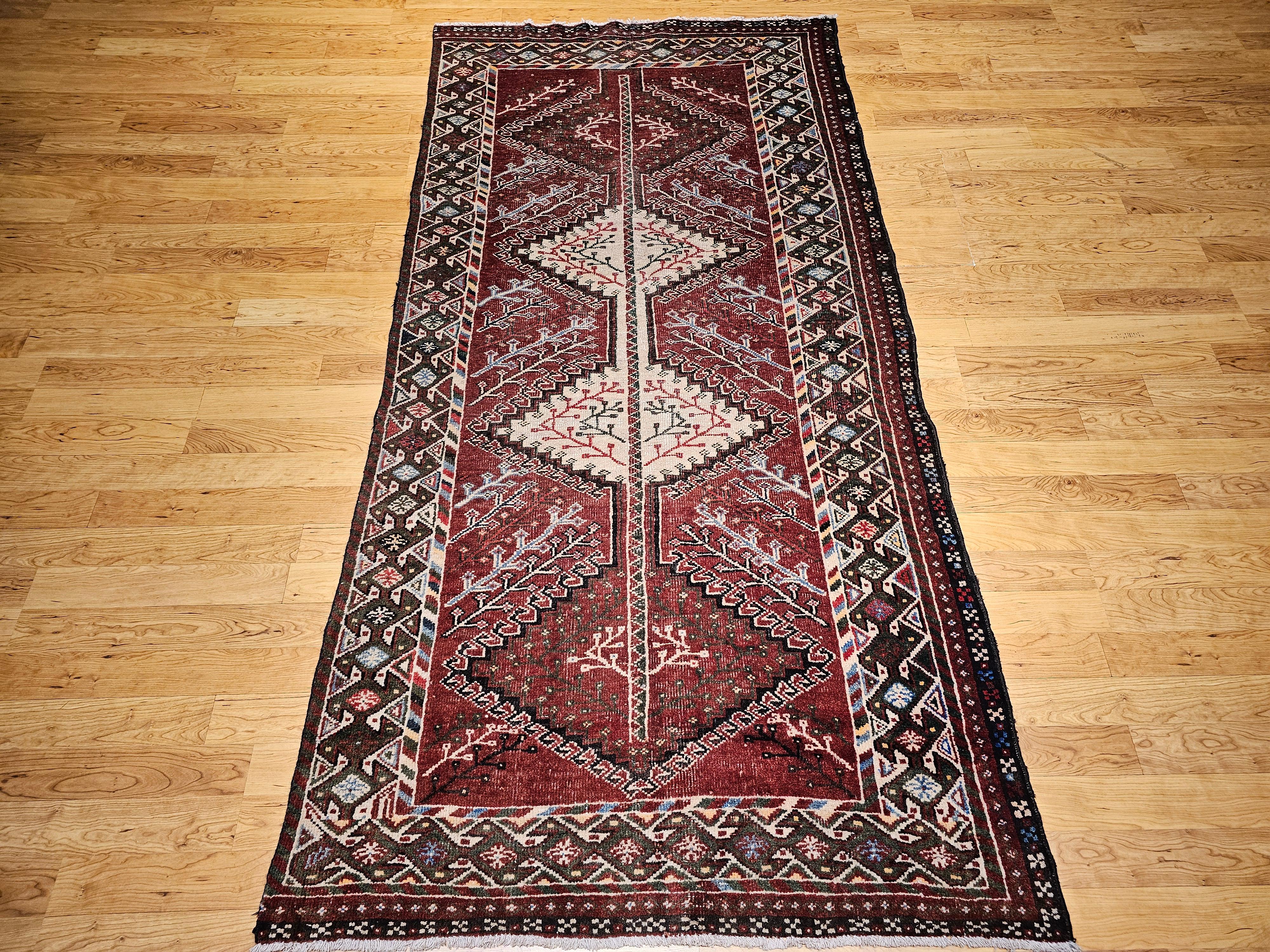 Vintage Persian Shiraz area rug / wide runner from Southwestern Persia comes in a rich burgundy color background. The main design of this vintage Shiraz rug is a connected series of small medallions containing vine patterns. The border in dark green