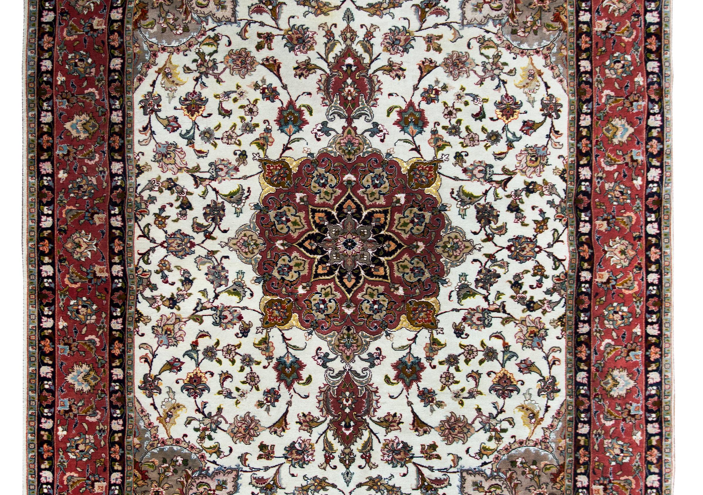 Un incroyable tapis persan Tabriz de la fin du 20e siècle, noué à la main en soie et en laine, avec un grand médaillon floral central vivant au milieu d'un champ de vignes et de fleurs tourbillonnantes, et entouré d'une large bordure à motifs