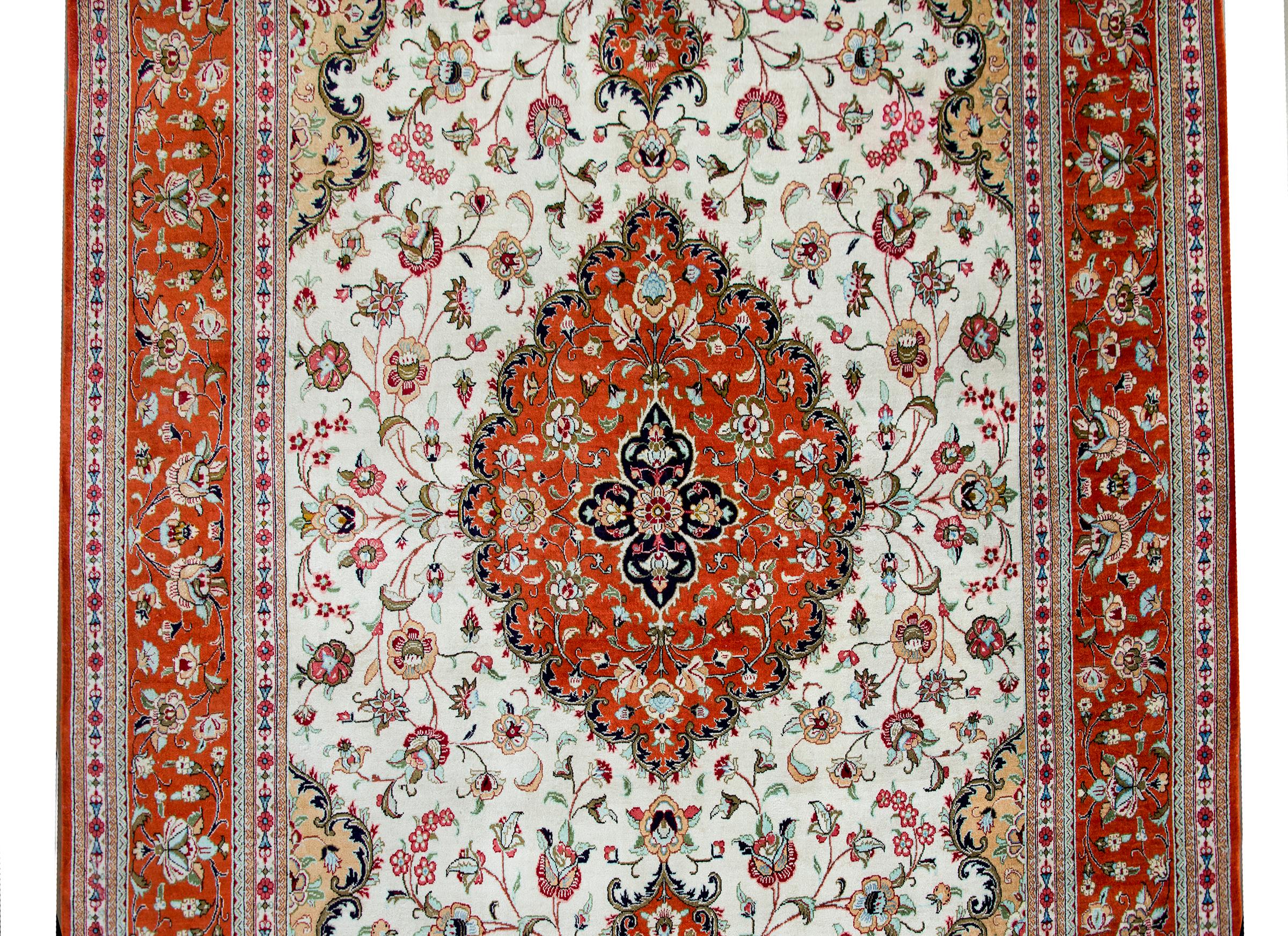A stunning late 20th century Persian Qum 100% silk rug with a large central floral medallion floating amidst a field of more stylized flowers and scrolling vines, and surrounded by a wide border with more repeated flowers and vines, and all woven in