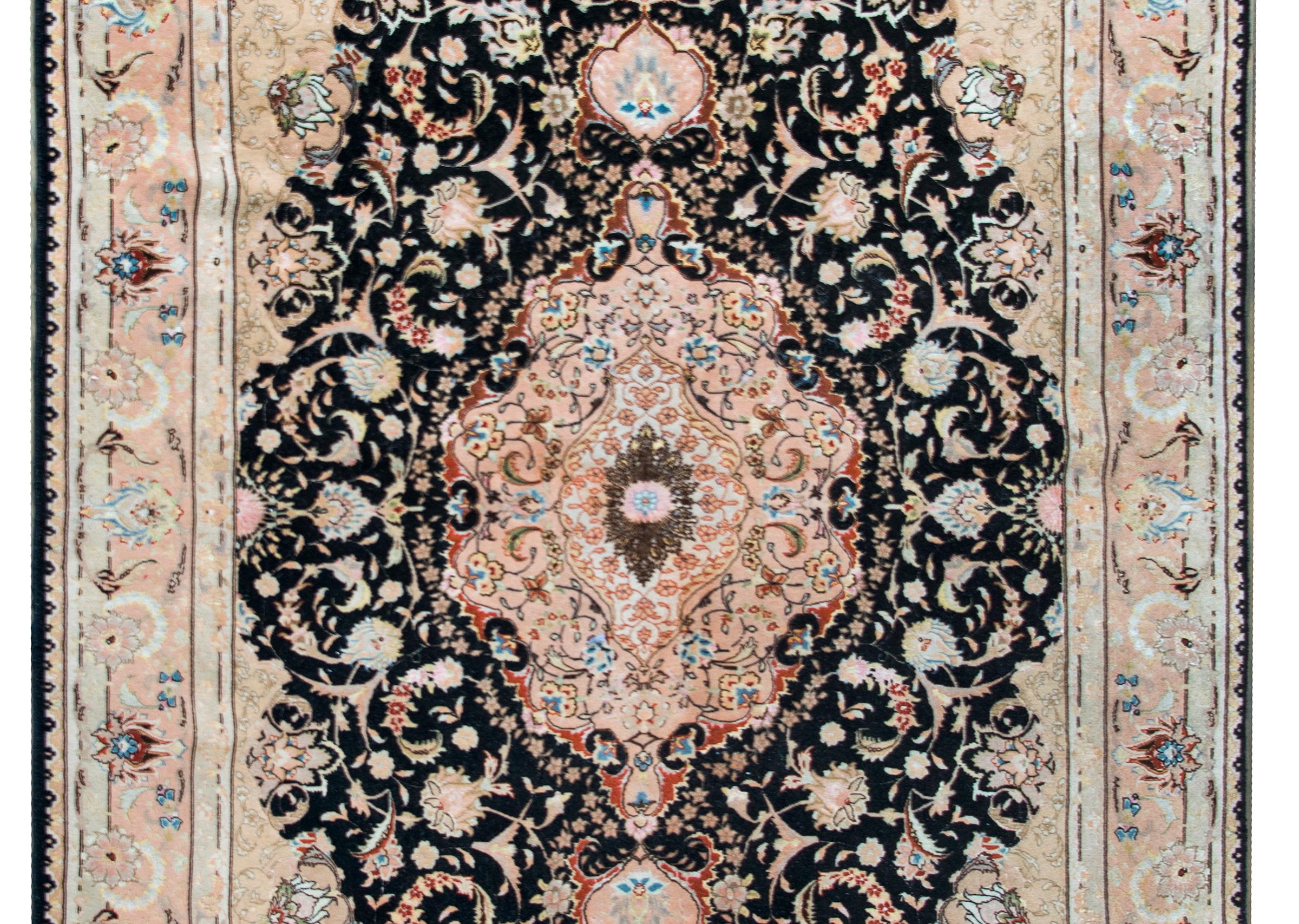A fantastic late 20th century Persian silk and wool Tabriz rug with a large central floral medallion living amidst even more scrolling vines and stylized flowers, and surrounded by a wide repeated floral patterned border.