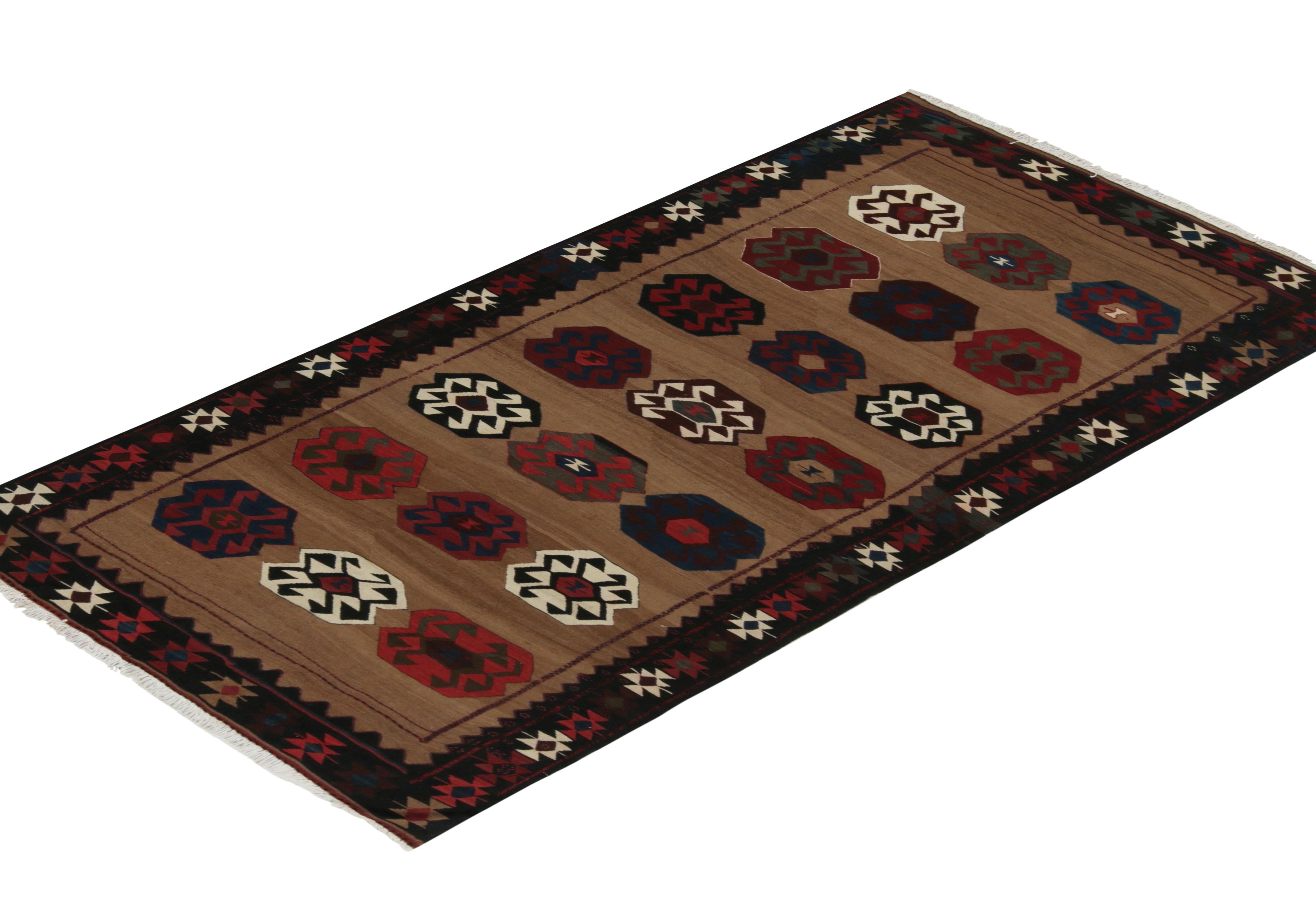 This vintage 5x9 Persian kilim is a unique tribal rug for its period, handwoven in wool circa 1950-1960.

Further on the Design:

A brown open field hosts repeated medallions with ram’s horn motifs, and an emphasis on red, blue, black, and white