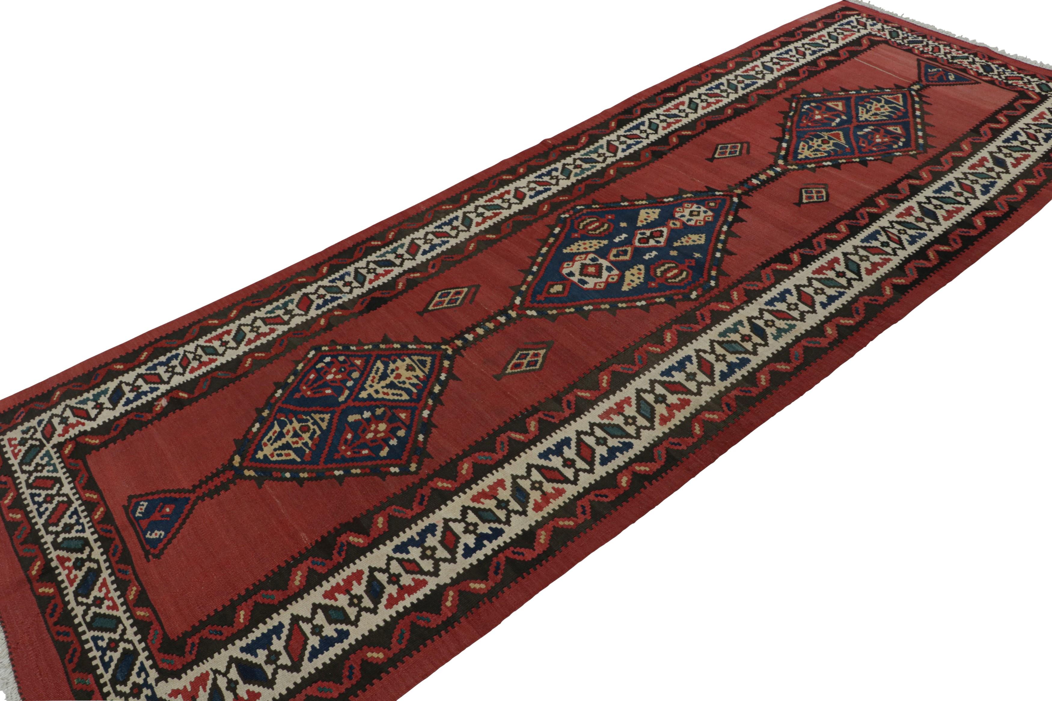 Dieser handgewebte Wollteppich (ca. 1950-1960) im Format 5 x 12 cm aus einem persischen Stammes-Kilim zeichnet sich durch detaillierte geometrische Muster in Beige/Braun und Blau in den Bordüren und Medaillons sowie durch ein sattes rotes Feld aus.
