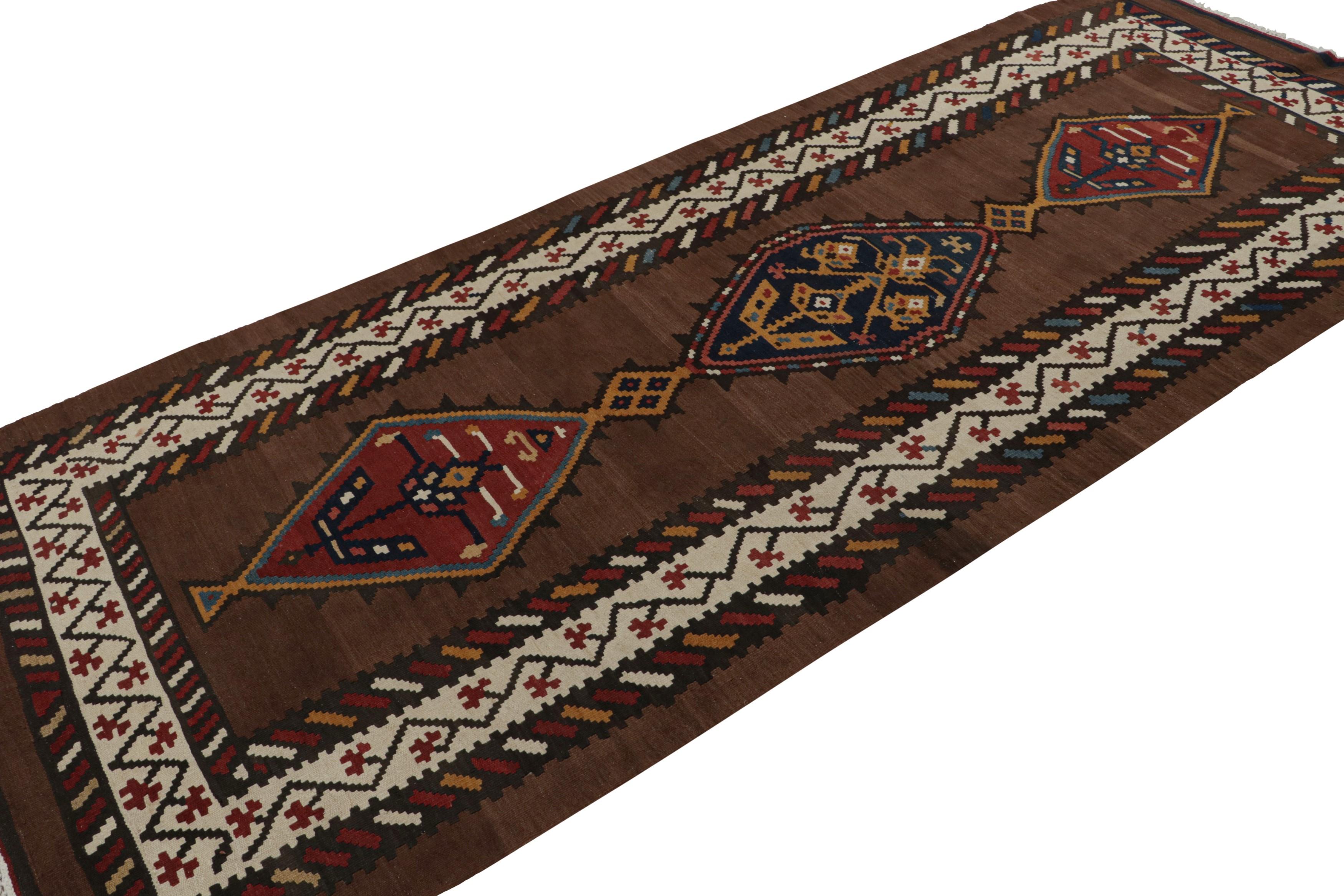 Handwoven in wool, circa 1950-1960, this 5x11 Persian tribal Kilim rug, features intricately detailed geometric patterns in beige, red and blue, in the borders and medallions, and a rich chocolate brown field.  

On the Design: 

A special piece in