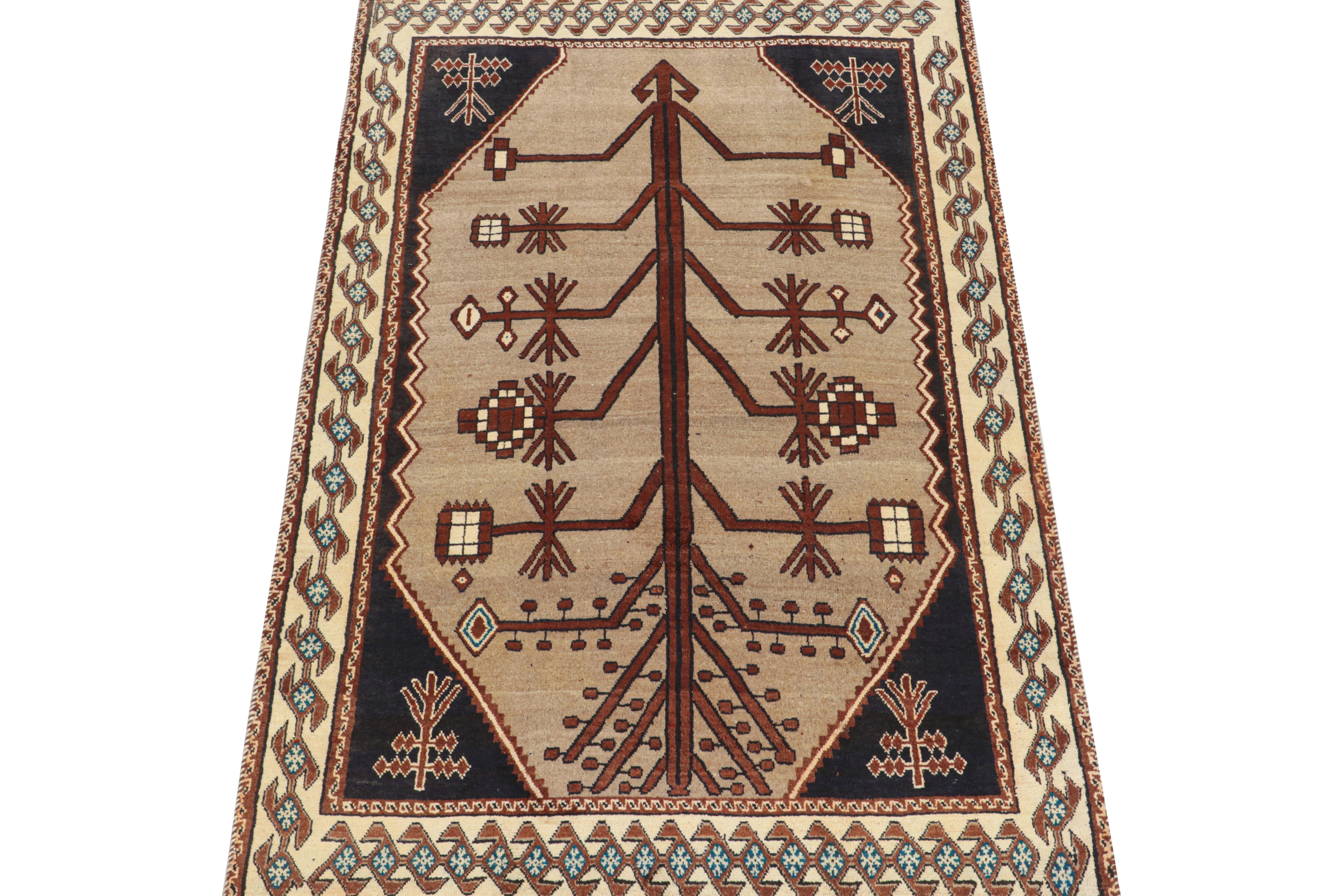 This vintage 5x8 Persian rug is a mid-century tribal piece, hand-knotted in wool circa 1950-1960.

Its design enjoys a medallion pattern in chocolate brown that resembles a primitivist tree depiction on a beige background. Navy blue, off-white,
