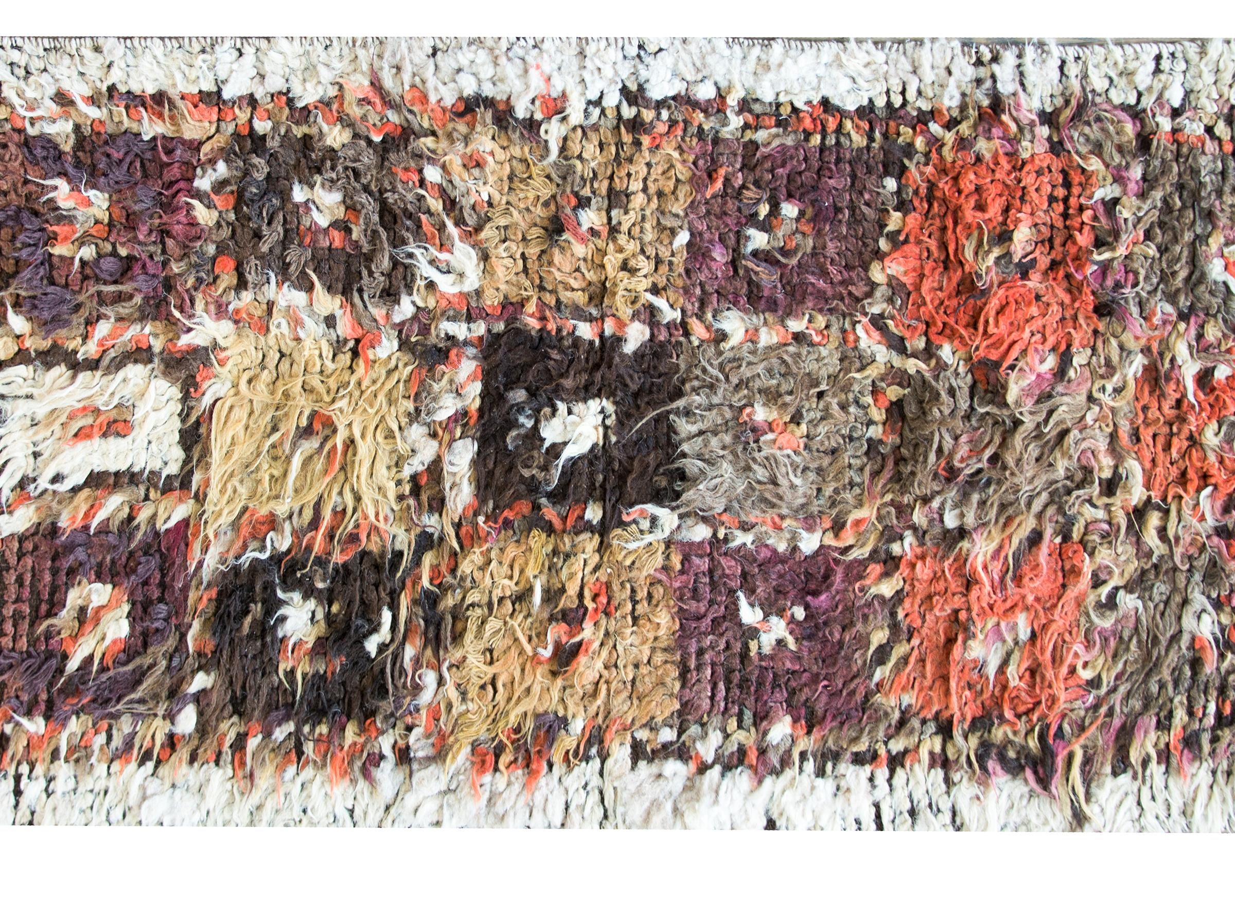 A bold vintage Persian Tulu rug with a patchwork pattern of orange, brown, gray, and gold squares, woven with a long shaggy wool.