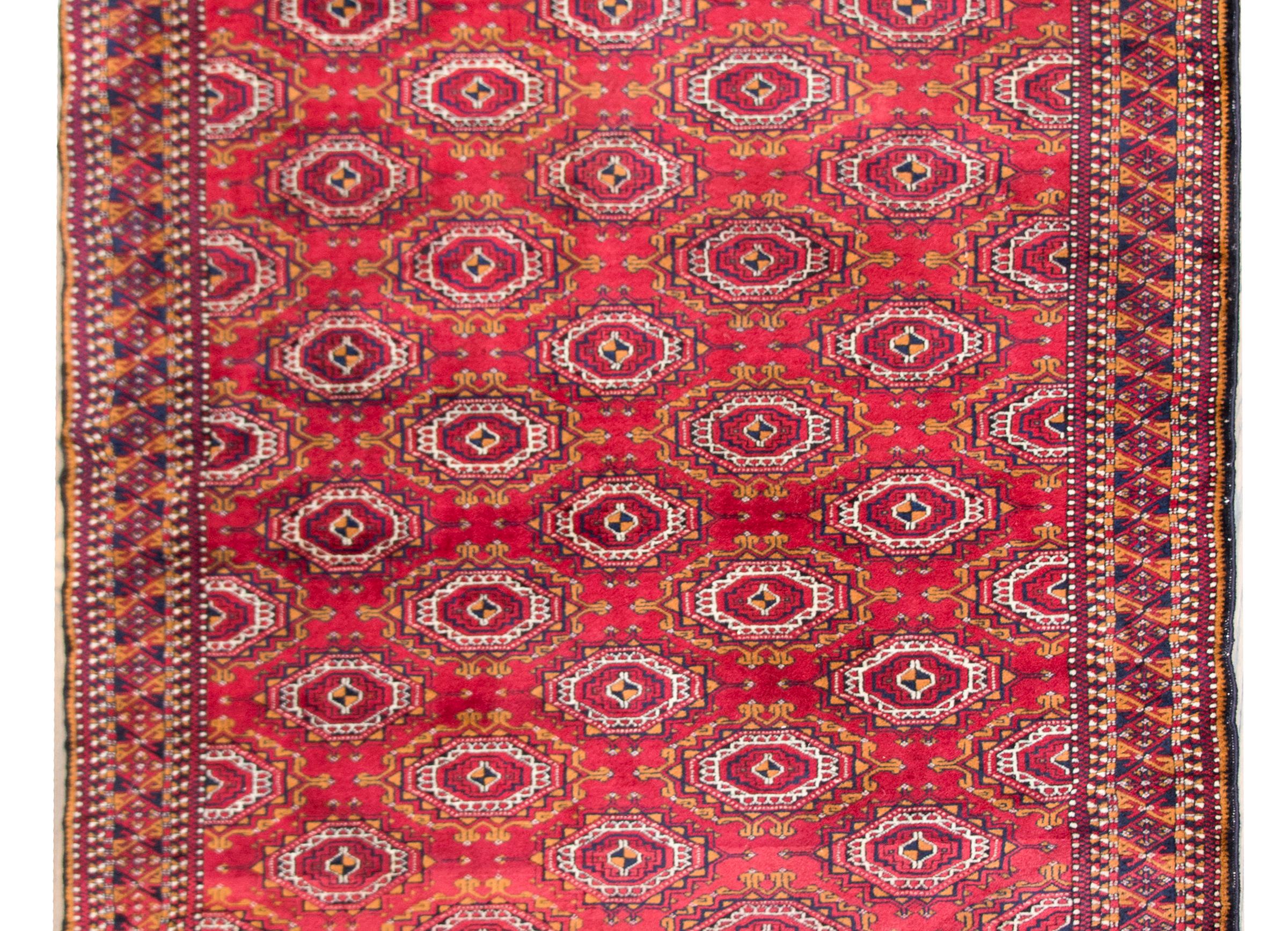 A wonderful late 20th century Persian Turkmen rug with an all-over stylized floral pattern surrounded by a complex border with multiple petite geometric and stylized floral patterns, and all woven in crimson, gold, black, and white wool.