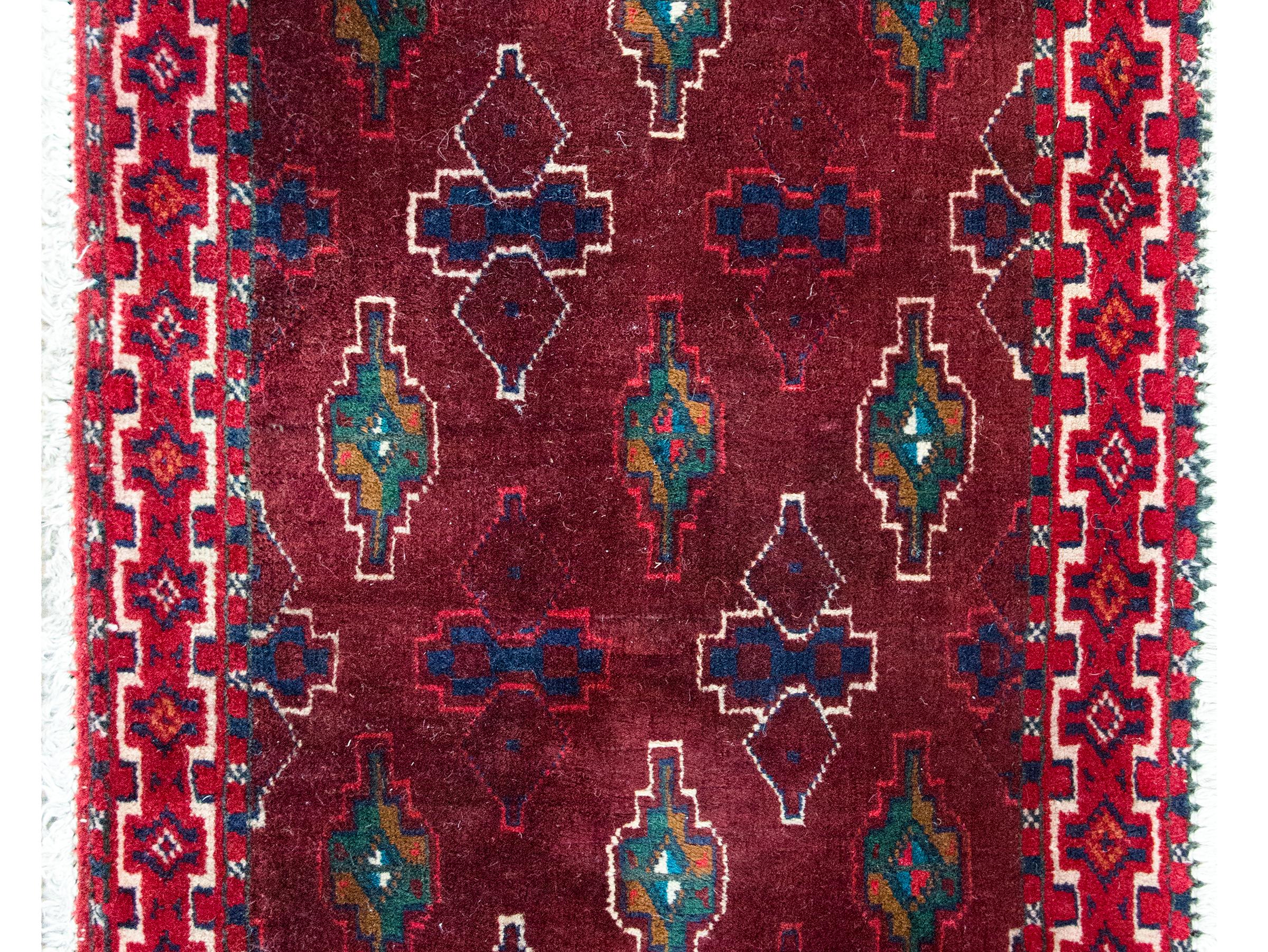 Charmant petit tapis persan turkmène dont le champ est couvert d'un motif tribal répété et entouré d'une bordure à motifs géométriques, le tout tissé dans de riches laines cramoisies, indigos, vertes, dorées et blanches.