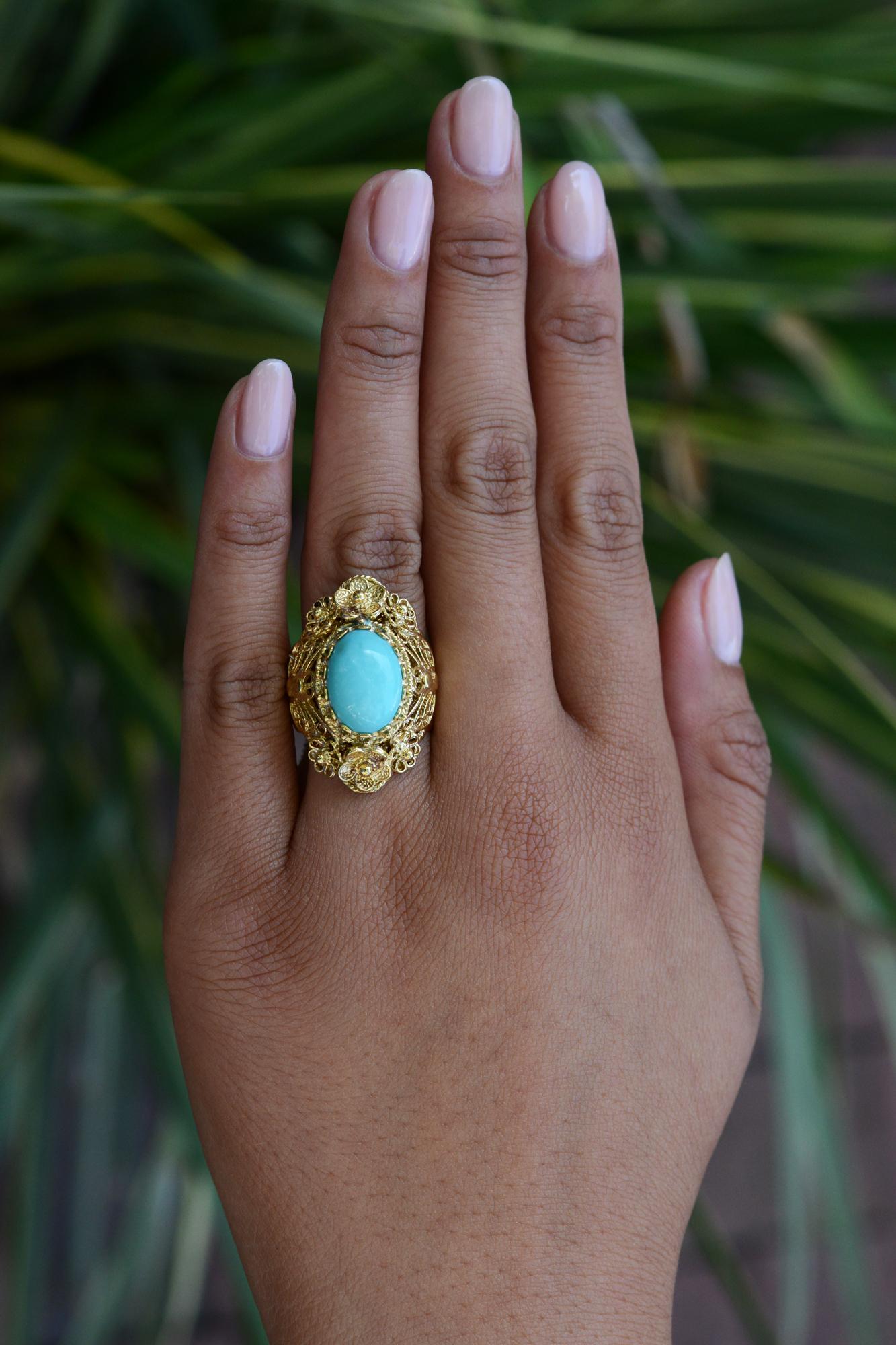 This vintage cocktail ring exhibits extensive craftsmanship and a luxurious, opulent, Persian turquoise showcased in the center. The rich 14k yellow gold portrays incredibly ornate floral motifs throughout the entirety of the ring. Featuring a