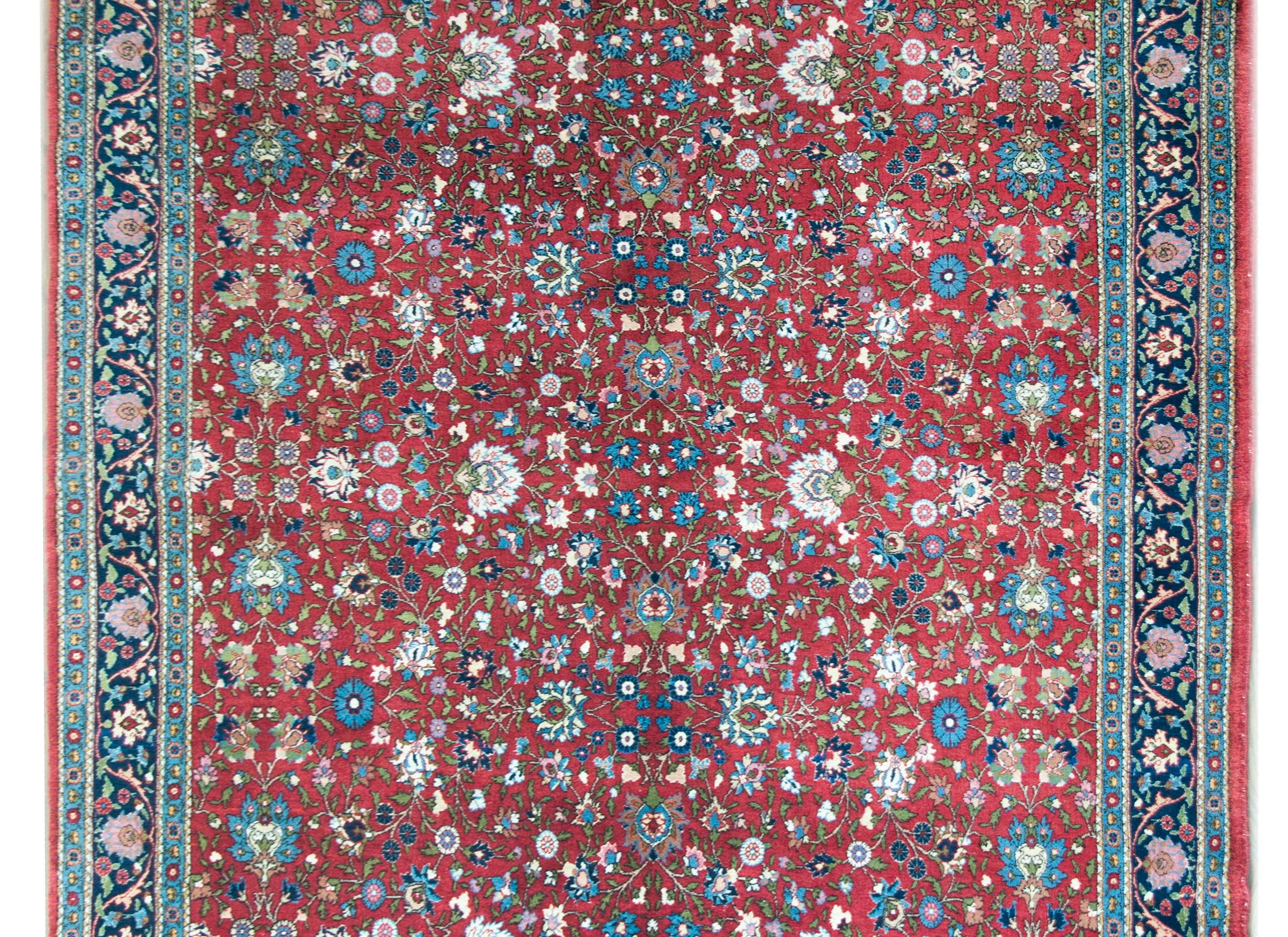 A wonderful mid-20th century Persian Varamin rug with an all-over mirrored trellis floral pattern with large-scale flowers and scrolling vines woven in light and dark indigo, green, pink, and white, set against a crimson background.  The border is