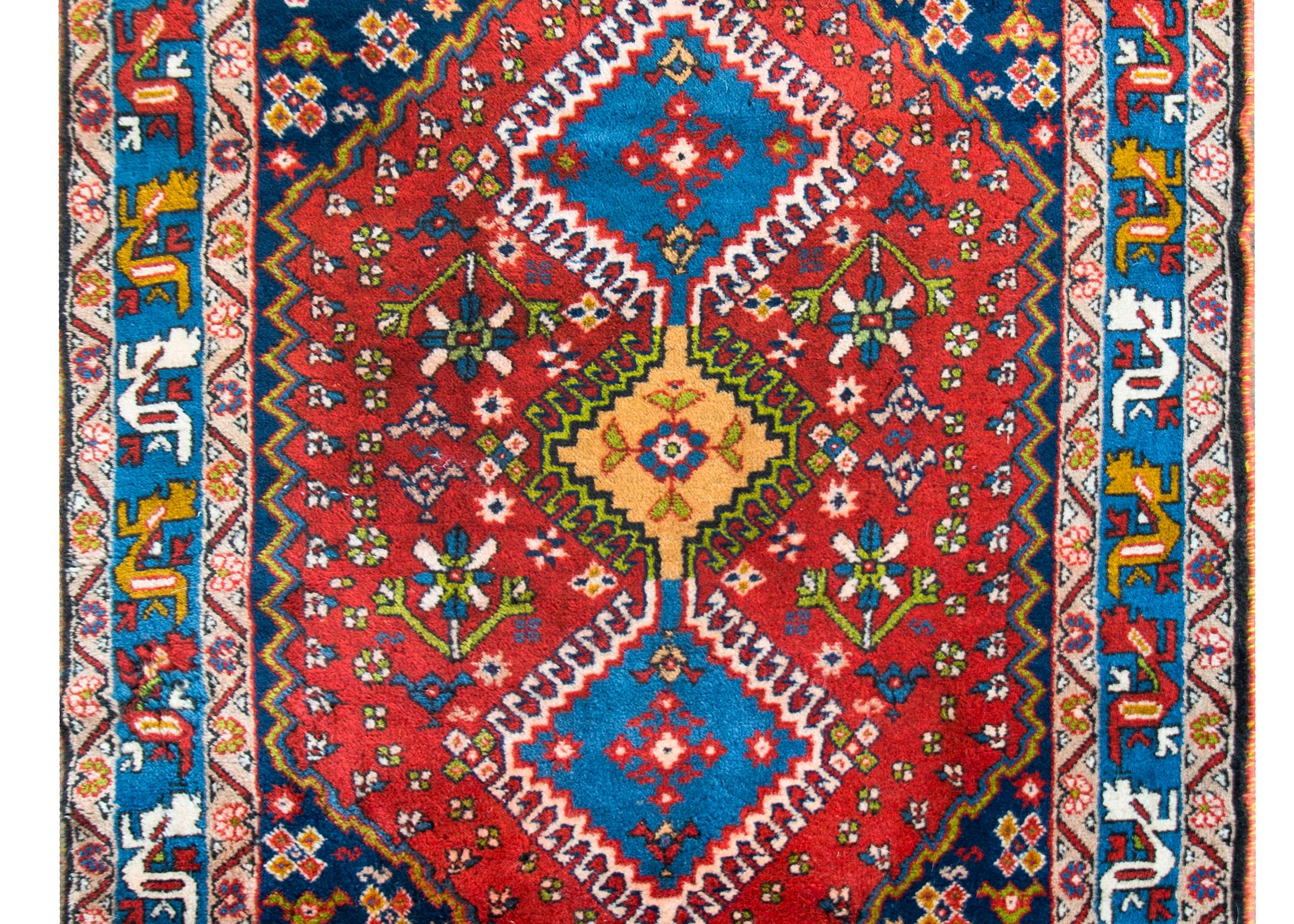 Tapis persan Yallameh du milieu du 20e siècle, audacieux et ludique, avec trois grands médaillons centraux en forme de diamant, entourés de vignes stylisées en spirale, et vivant au milieu d'un champ de fleurs, le tout entouré d'une large bordure de