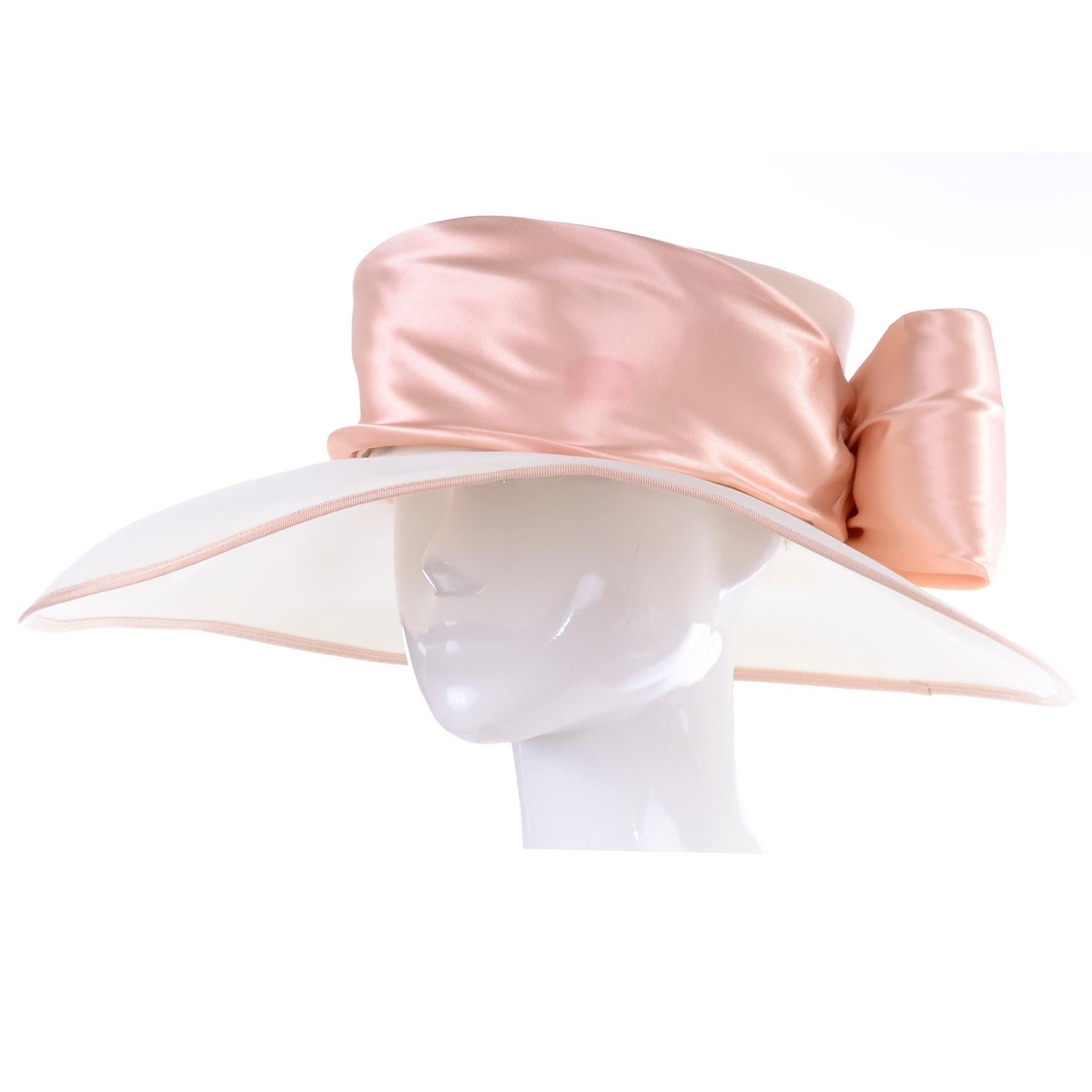 This is a beautiful curved wide brim hat by Peter Bettley with peach pink trim and a large satin ribbon with a bow in the back. The brim is cream and the top of the hat is also a neutral peach pink color! Milliner Peter Bettley was trained as an
