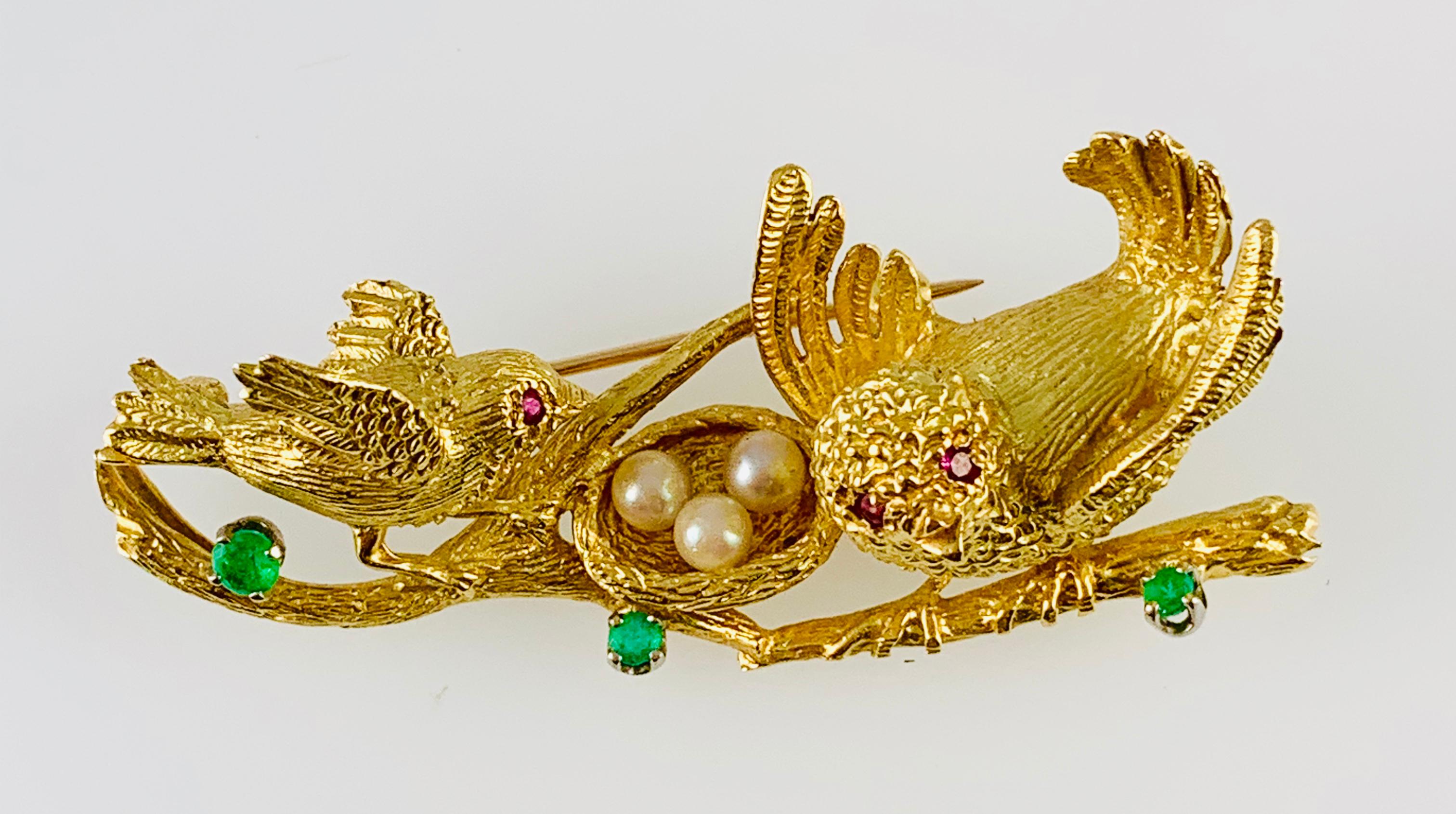 What a beautiful and whimsical Peter Linderman Brooch!. This Vintage piece dates Circa 1970 and is made in 18K yellow Gold. It features two parent birds standing on tree branches watching over their pearl eggs in the nest. Each Bird has Rubies for