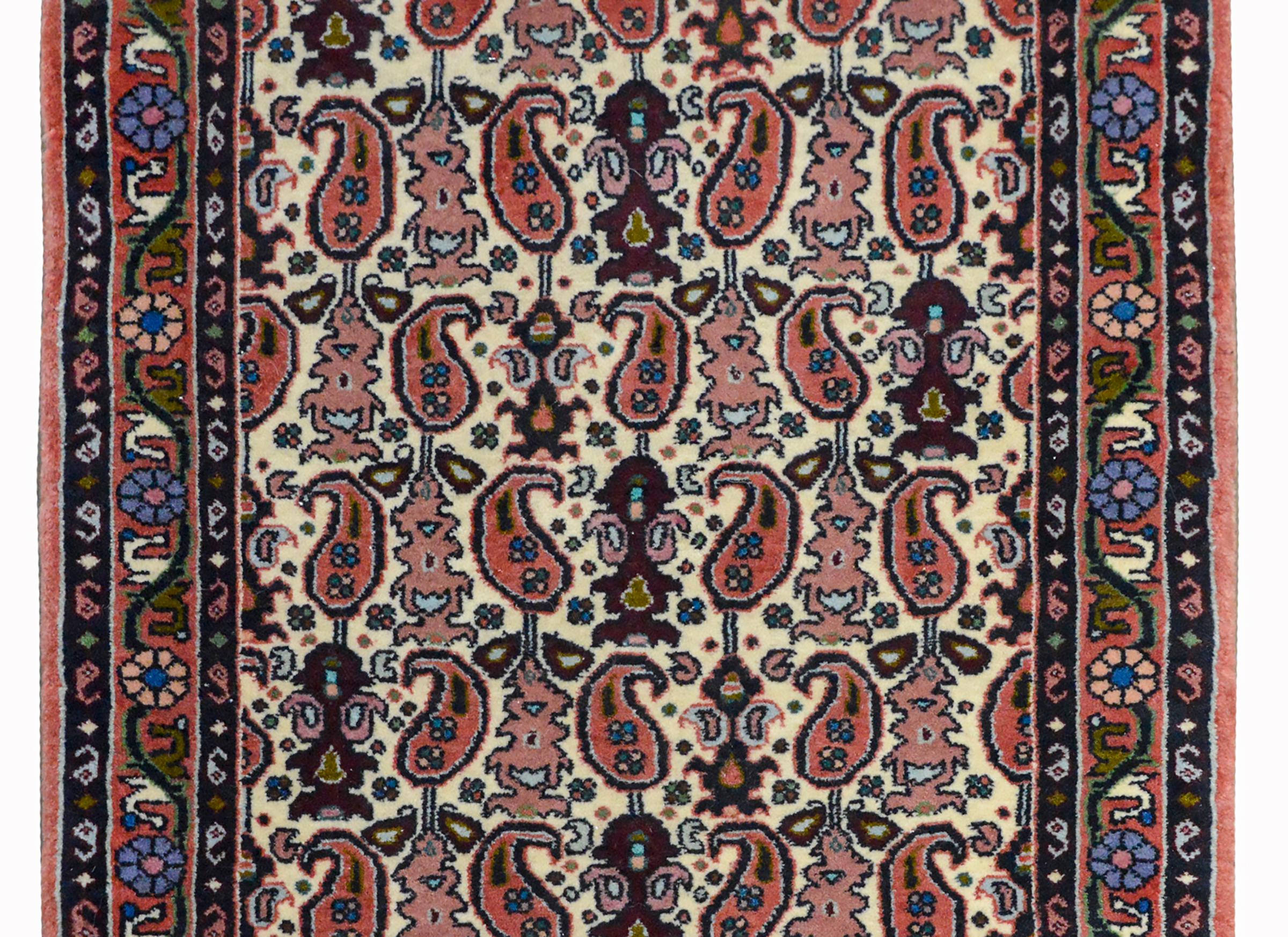 A wonderful vintage petite Persian Bidjar rug with an all-over paisley pattern woven in dark and light red, light indigo, and green against a cream colored background. The border is sweet, with a floral and scrolling vine flanked by a pair of petite