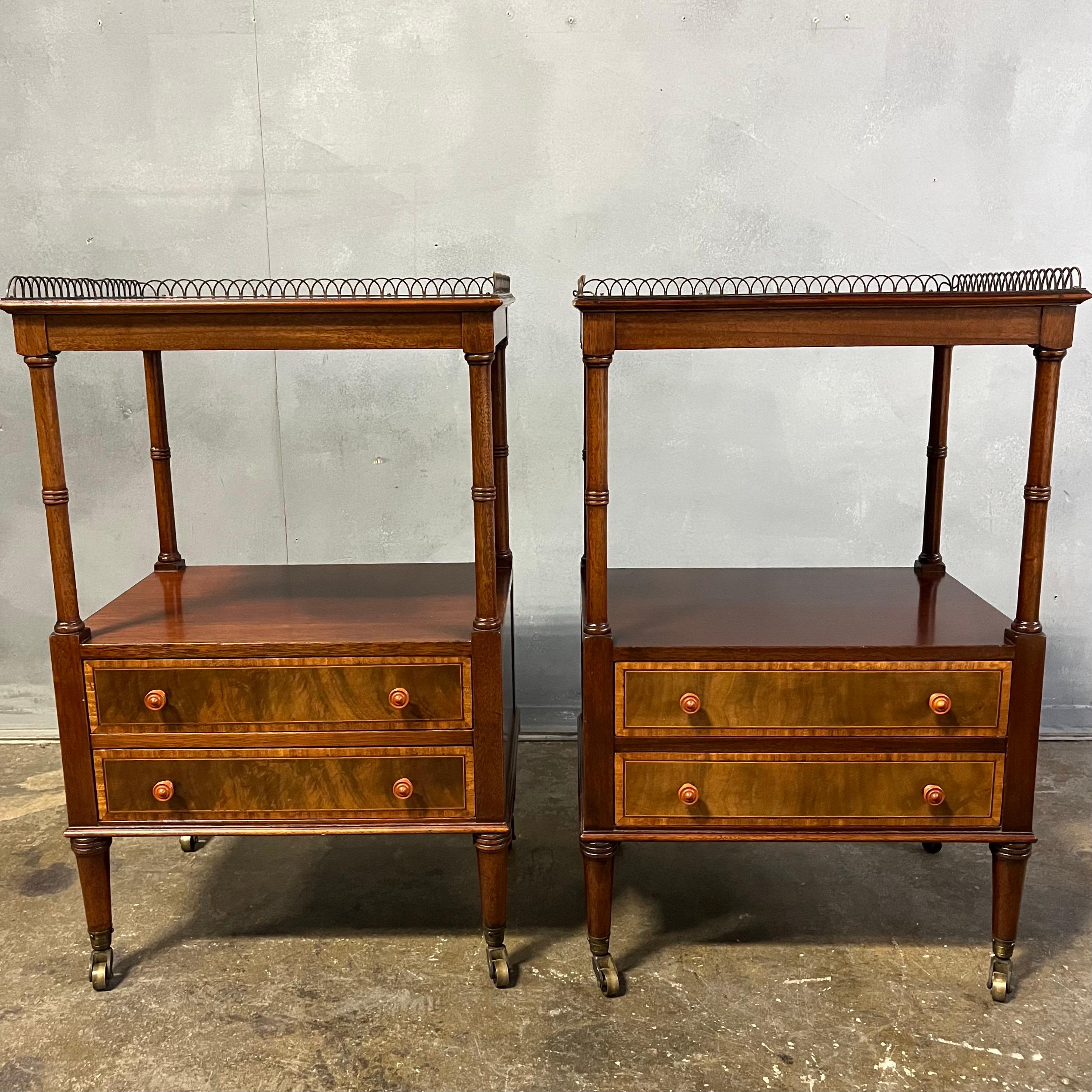 Gorgeous pair of bedside or end tables having a mahogany construction with olive burl wood inlay and a brass fence gallery. Featuring two drawers with open hole measuring a 10.5' height opening above drawers all standing on brass casters. We just