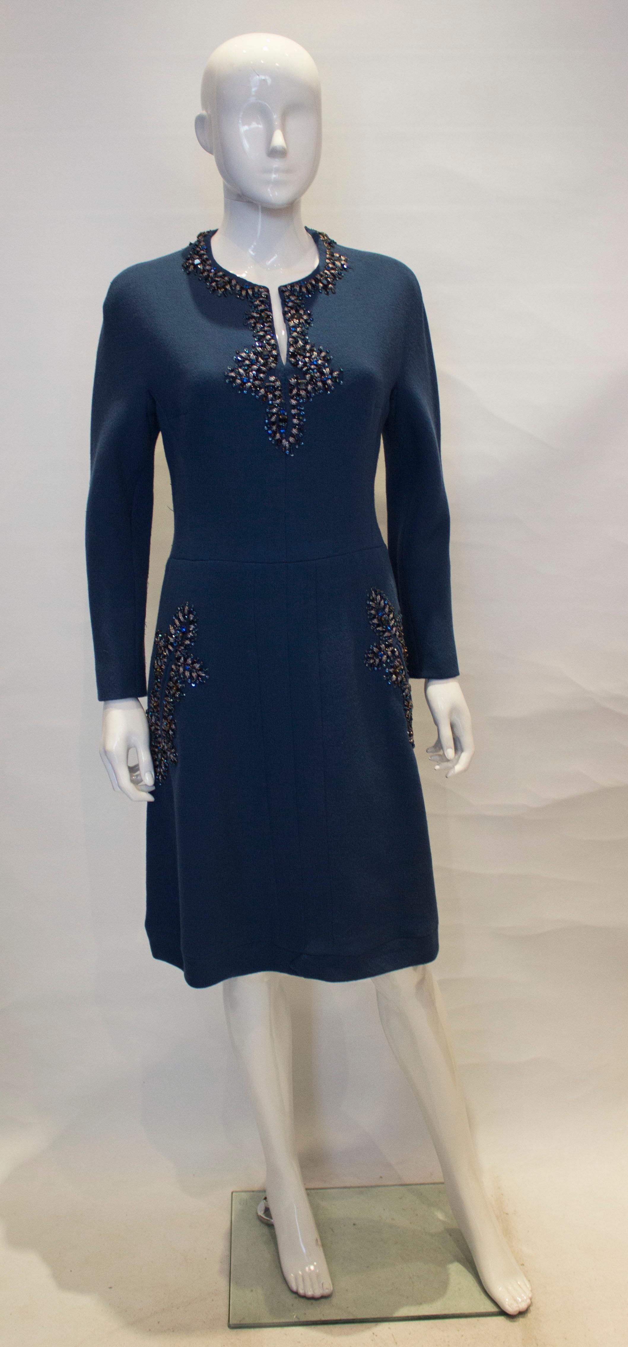 A chic vintage cocktail dress by Assutina Alta Moda.  In a petrol blue wool crepe, the dress has a v neckline, central back zip, flared skirt and two front pockets. There is wonderful embellishment around the necklline and pockets. 