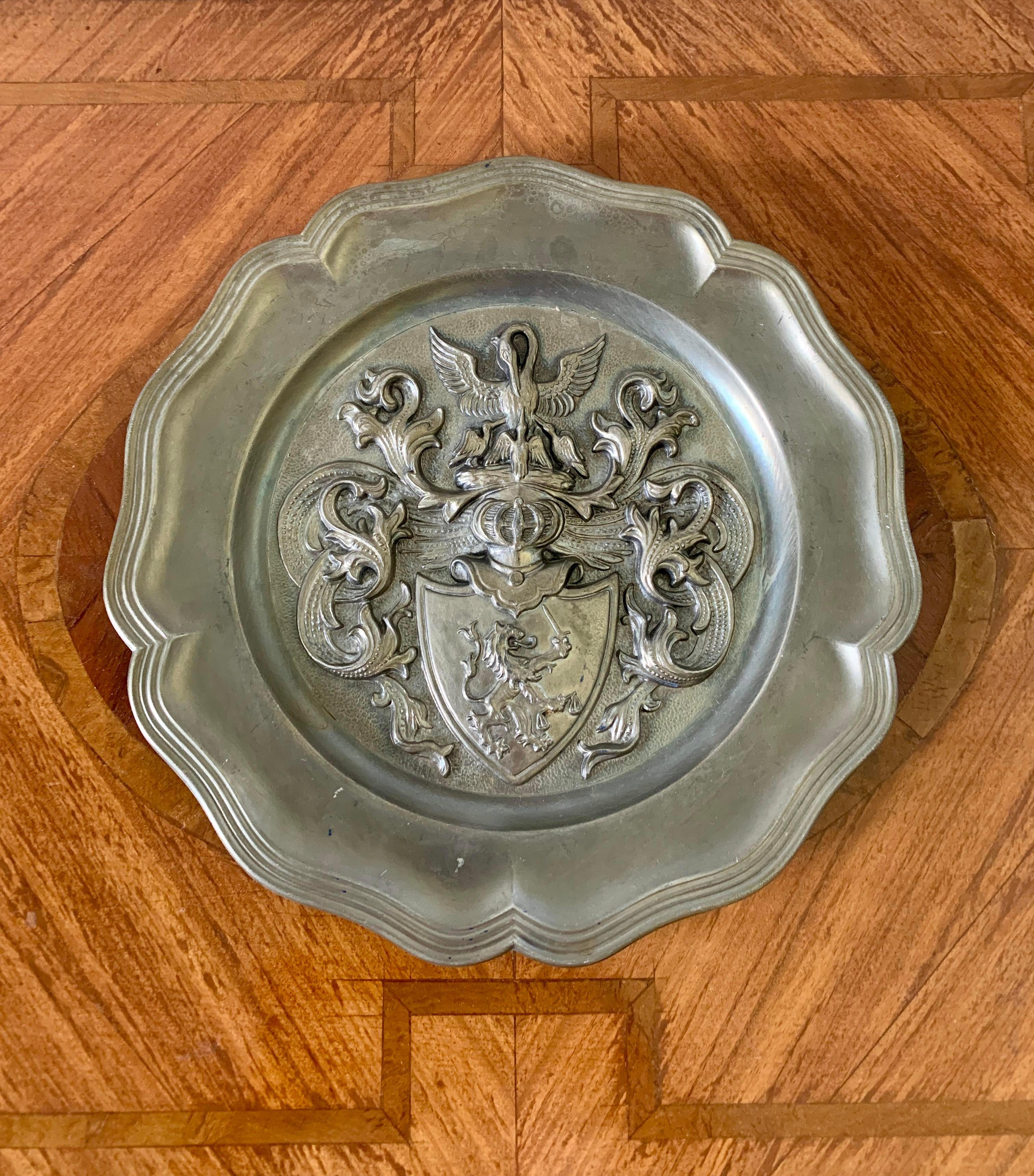 An early 20th century German pewter wall plate with a family crest consisting of a lion with sword on a shield culminating in a mother pelican feeding her babies. The symbolism of the mother pelican feeding her baby pelicans is part of an ancient