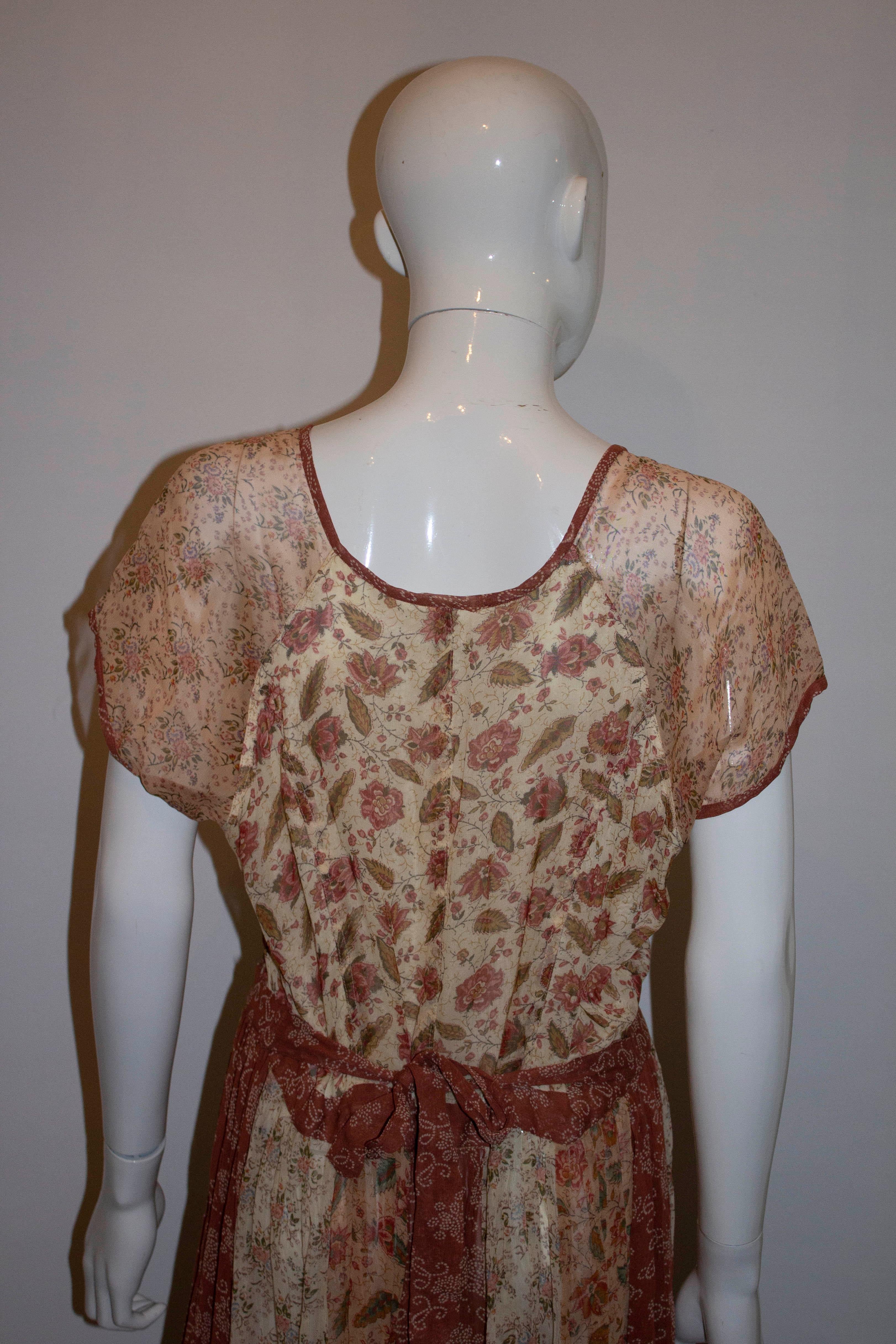 A lovely vintage floral dress by Phool, in a mix of green, red , beige and ivory. The dress has cap sleaves , a button front and self fabric tie belt at the back.  It is a wonderful mix of different panels of print with lace detail and one print on