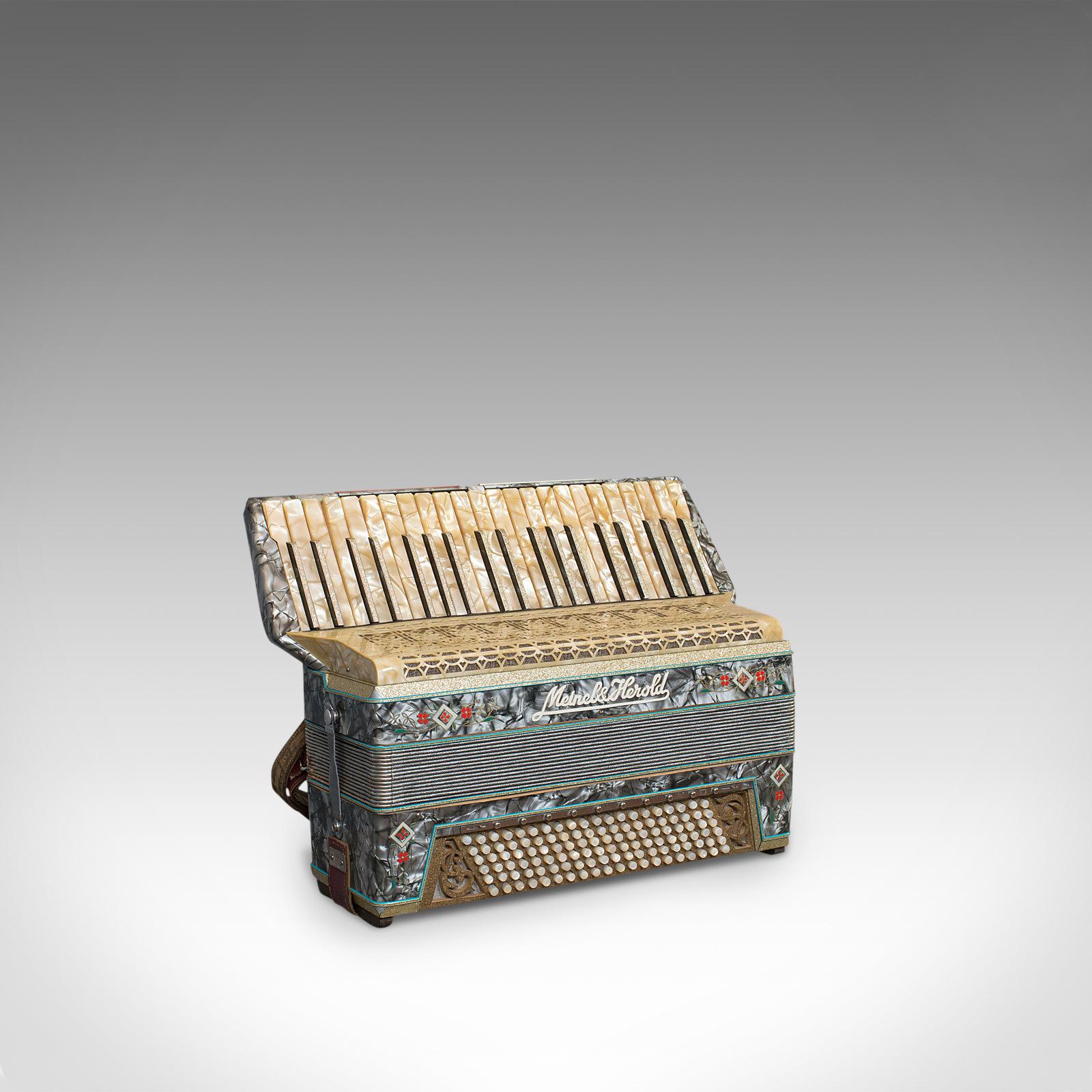 Il s'agit d'un accordéon piano vintage. Une caisse de résonance allemande en perles de Meinel et Herold avec anches Dix et étui, datant du milieu du 20e siècle, vers 1940.

Décoration abondante et étui d'origine
L'accordéon présente une patine