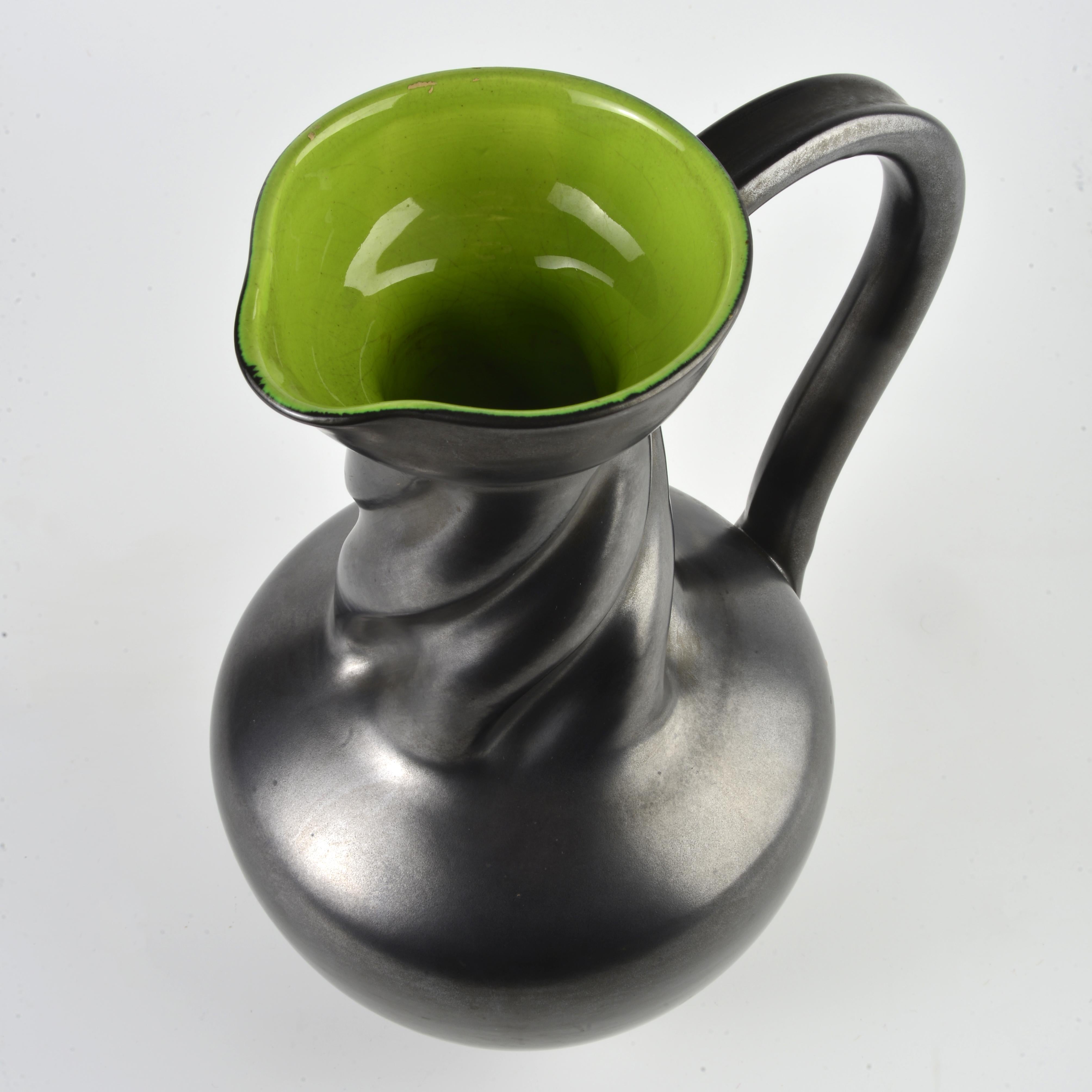 Glazed earthenware pitcher from the 1950s/60s by the Elchinger factory, grey/black satin glaze on the outside and bright green on the inside. H:29cm

The Elchinger factory, named after its creator, operated in Alsace from 1834 to 2016. At the