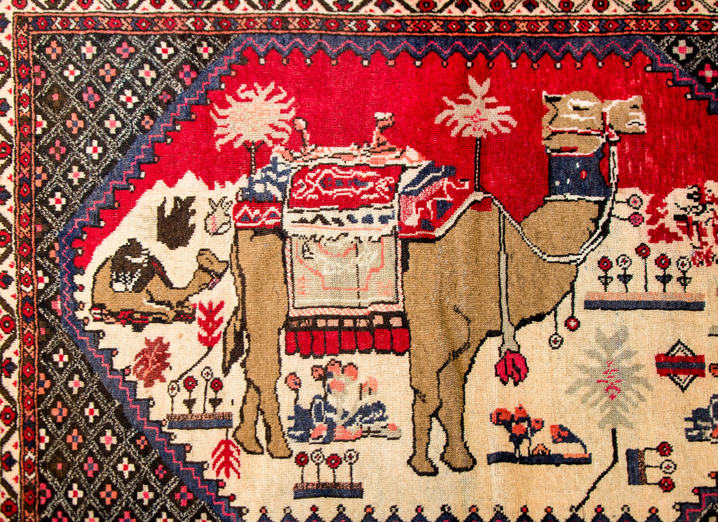 A wonderful vintage pictorial Persian Kelardasht rug with two camels, one kneeling and one standing, amidst a desert landscape with myriad flowering plants and trees. The border is composed with multiple petite flowers, with a complex border
