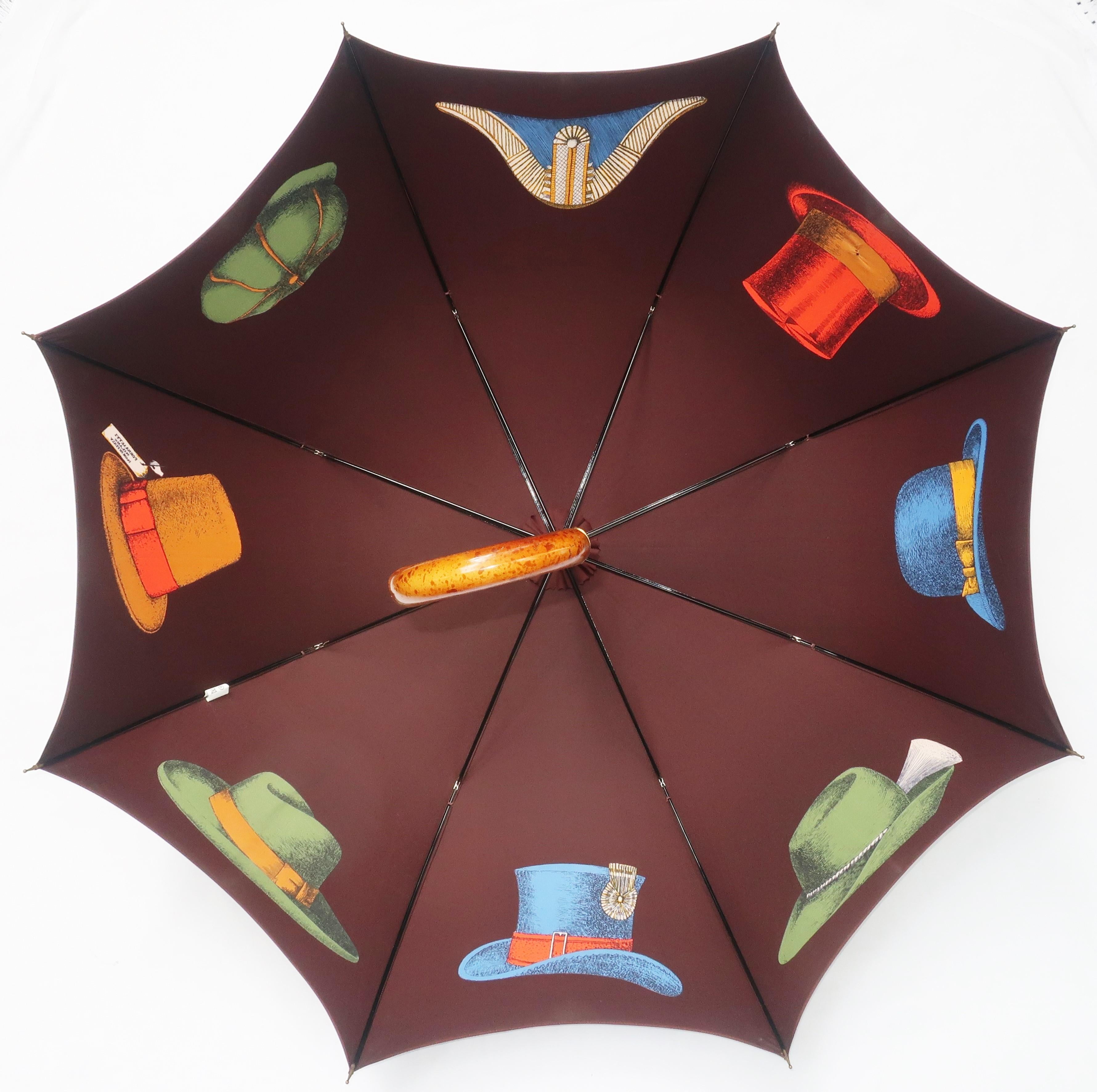 De la mente creativa de Piero Fornasetti... un elegante y gallardo paraguas marrón decorado con trampantojos de sombreros en tonos naranja, rojo, verde, azul y azul marino.  amarillo dorado.  Maravillosamente fabricado con eje de madera, mango
