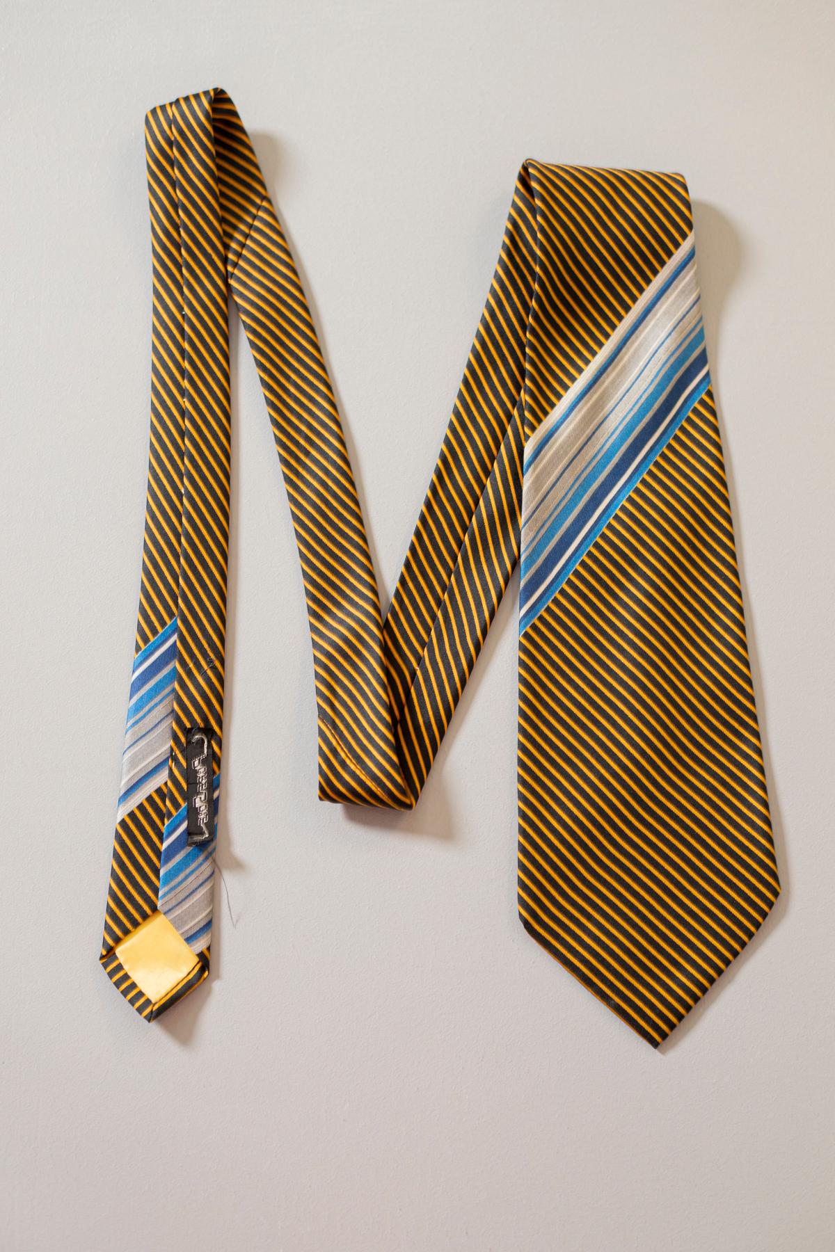 Vintage tie designed by Pierre Belmain, it is made of silk. Decorated with small yellow stripes on a black background and a large blue / gray script. With a very elegant and formal design, this tie is perfect for lovers of a classic taste, who want