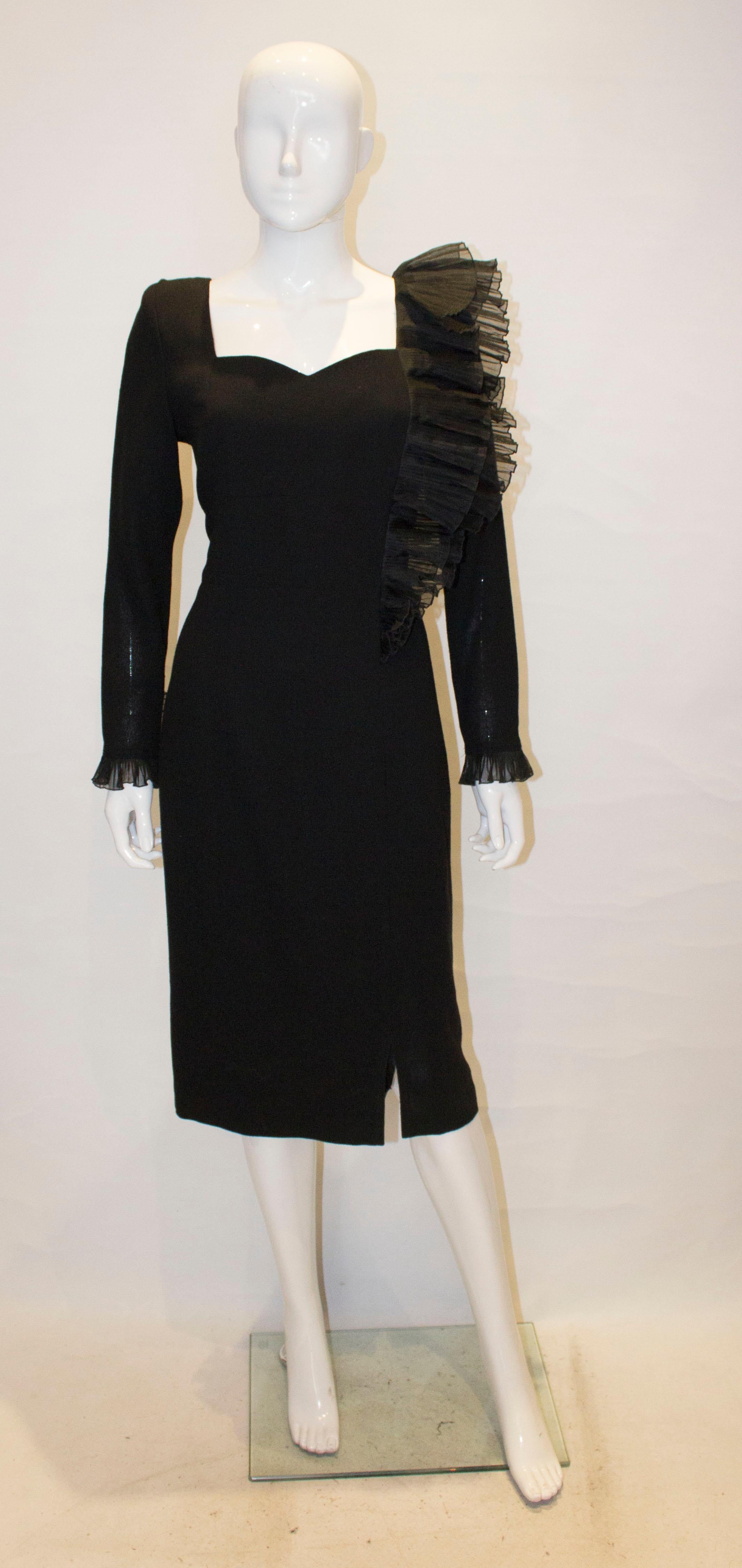 A vintage black wool cocktail dress by Pierre Cardin . The dress has a double ruffle detail on one side and over the shoulder and single ruffle detail on the cuff.  There is a 5 1/2'' slit at the front on one side and a central back zip. The dress