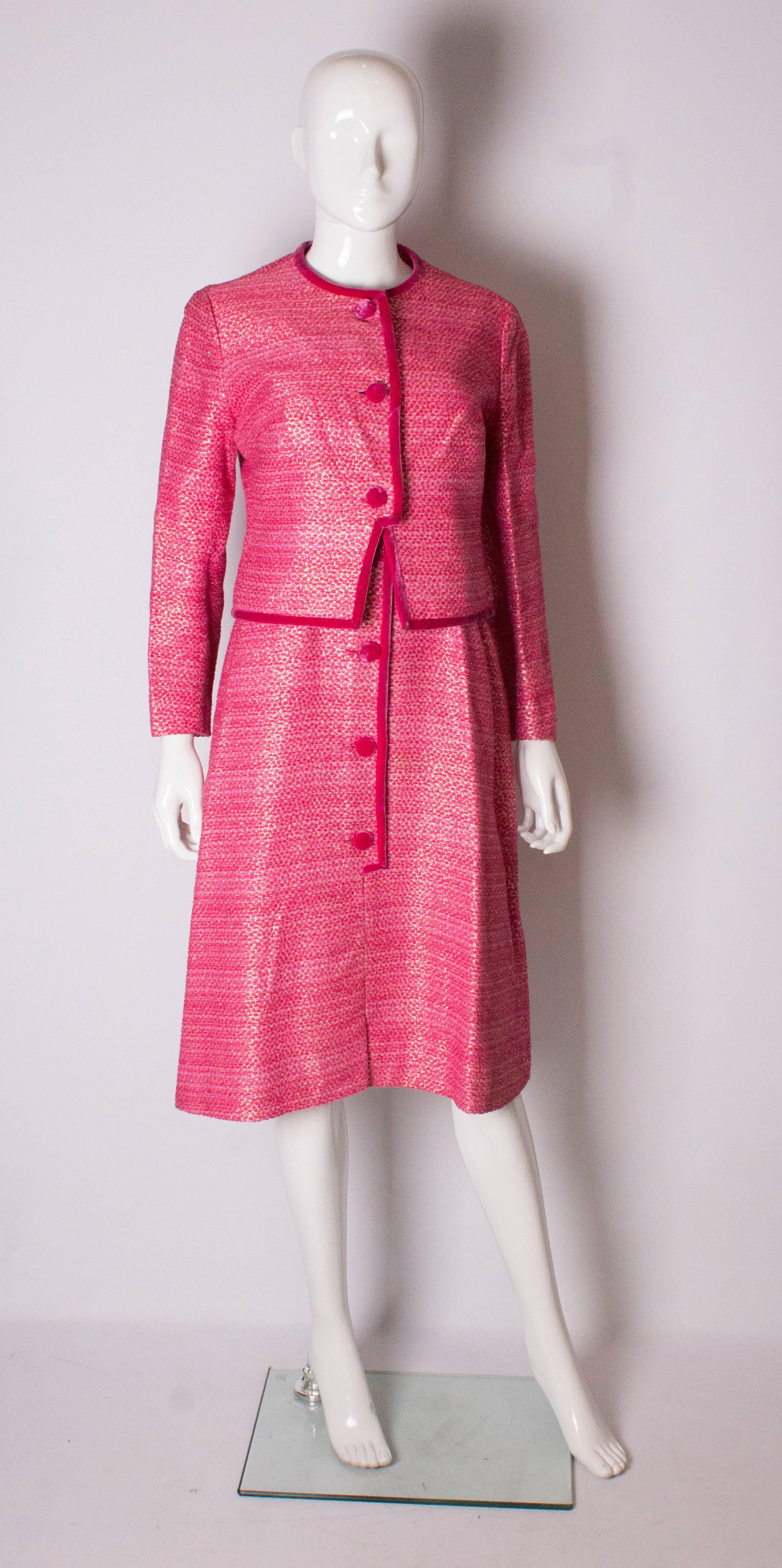 A chic, pink vintage  cocktail dress and jacket by Pierre Celeyre. The jacket has a round neck and is trimmed in pink velvet around the collar, front and hem. It has a three button central opening.
The dress has a pink satin bodice and side zip. The