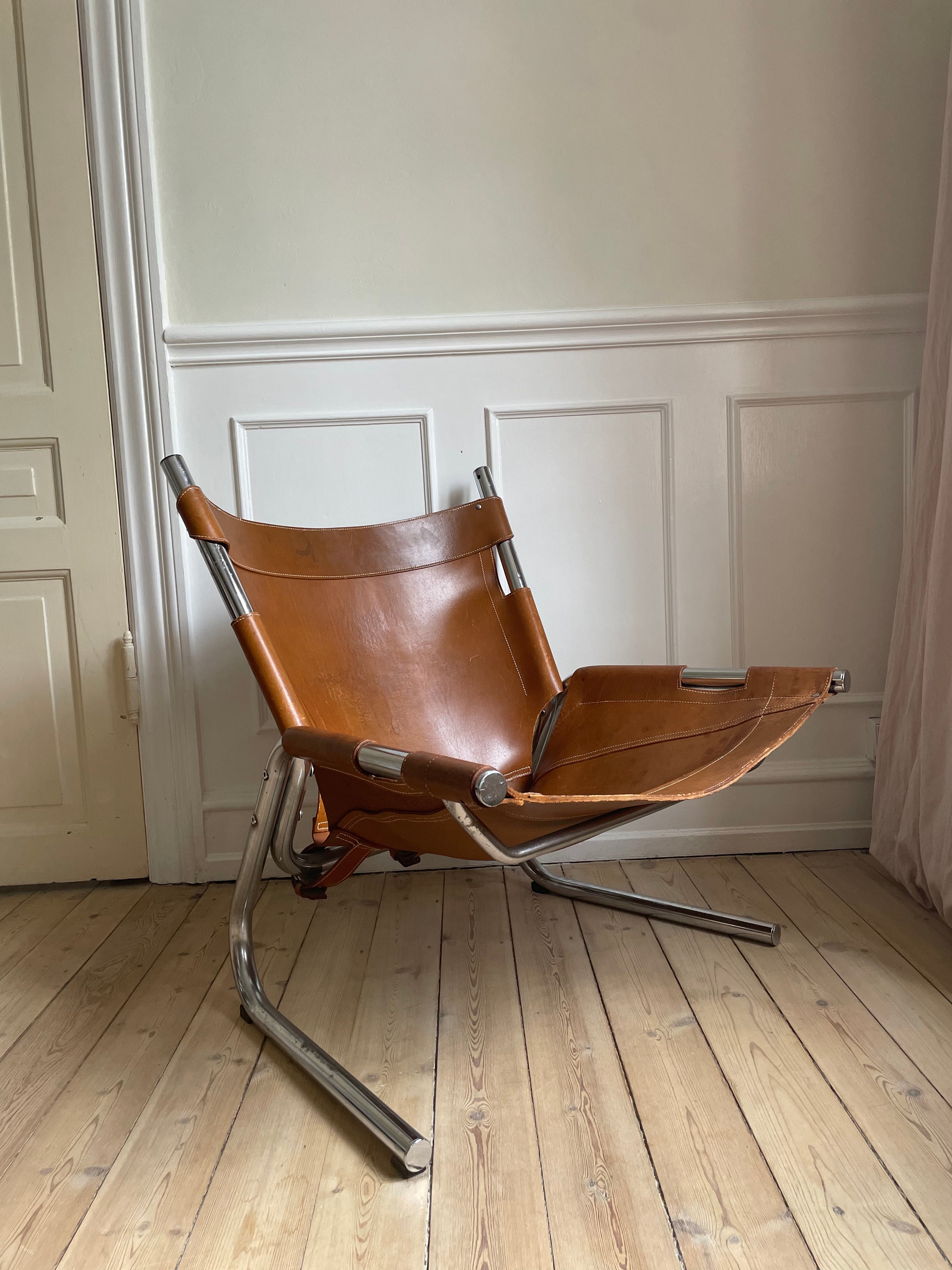 European midcentury modern leather sling lounge chair. Steel tube base with natural brown patinated cognac leather attached with metal buckle leather straps and light brown stitches. Scandinavian, Dutch or French design in the style of Pierre