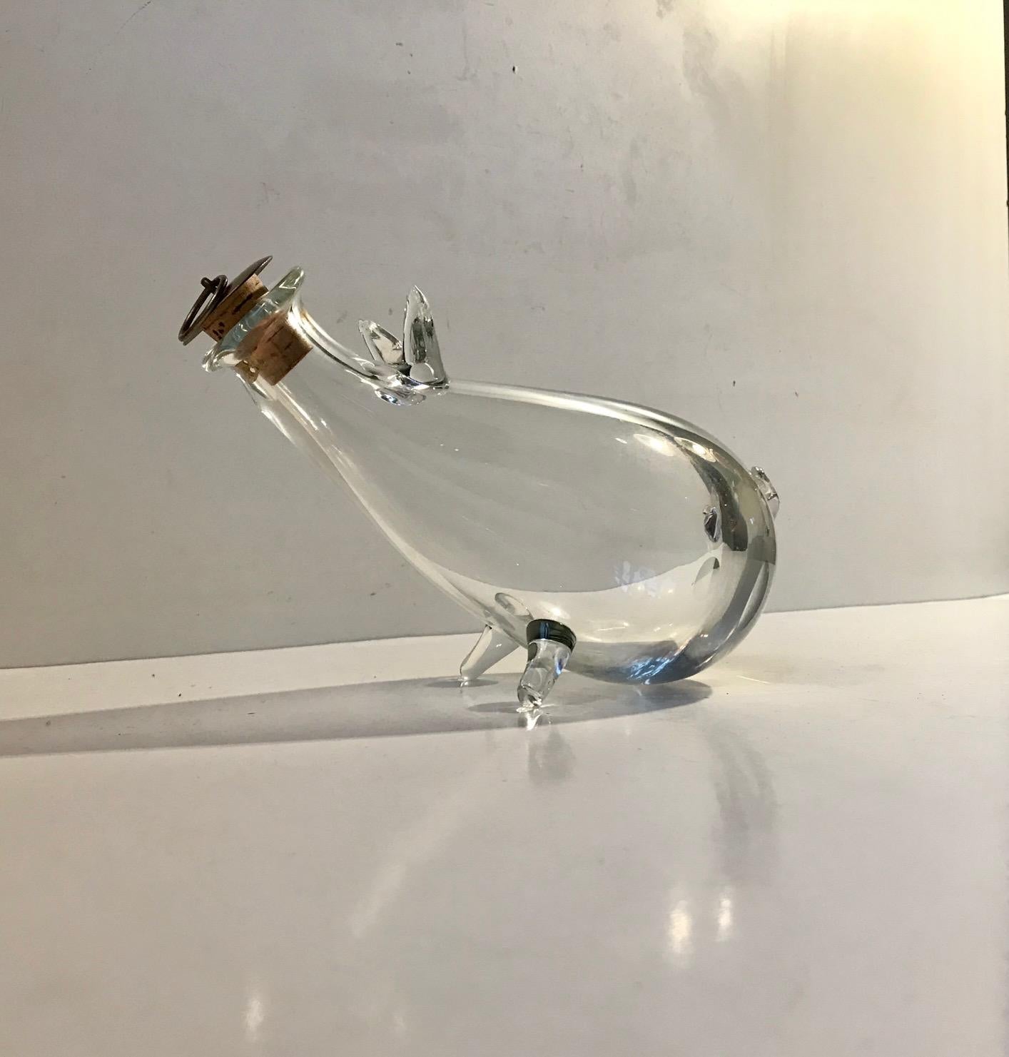 Small chubby decanter shaped as a pig. It is made from handblown glass with added pig attributes. It has its original stopper in brass and cork from Holmegaard. It was made at Holmegaard in Denmark during the 1960s. It can contain circa 0,6 liters.