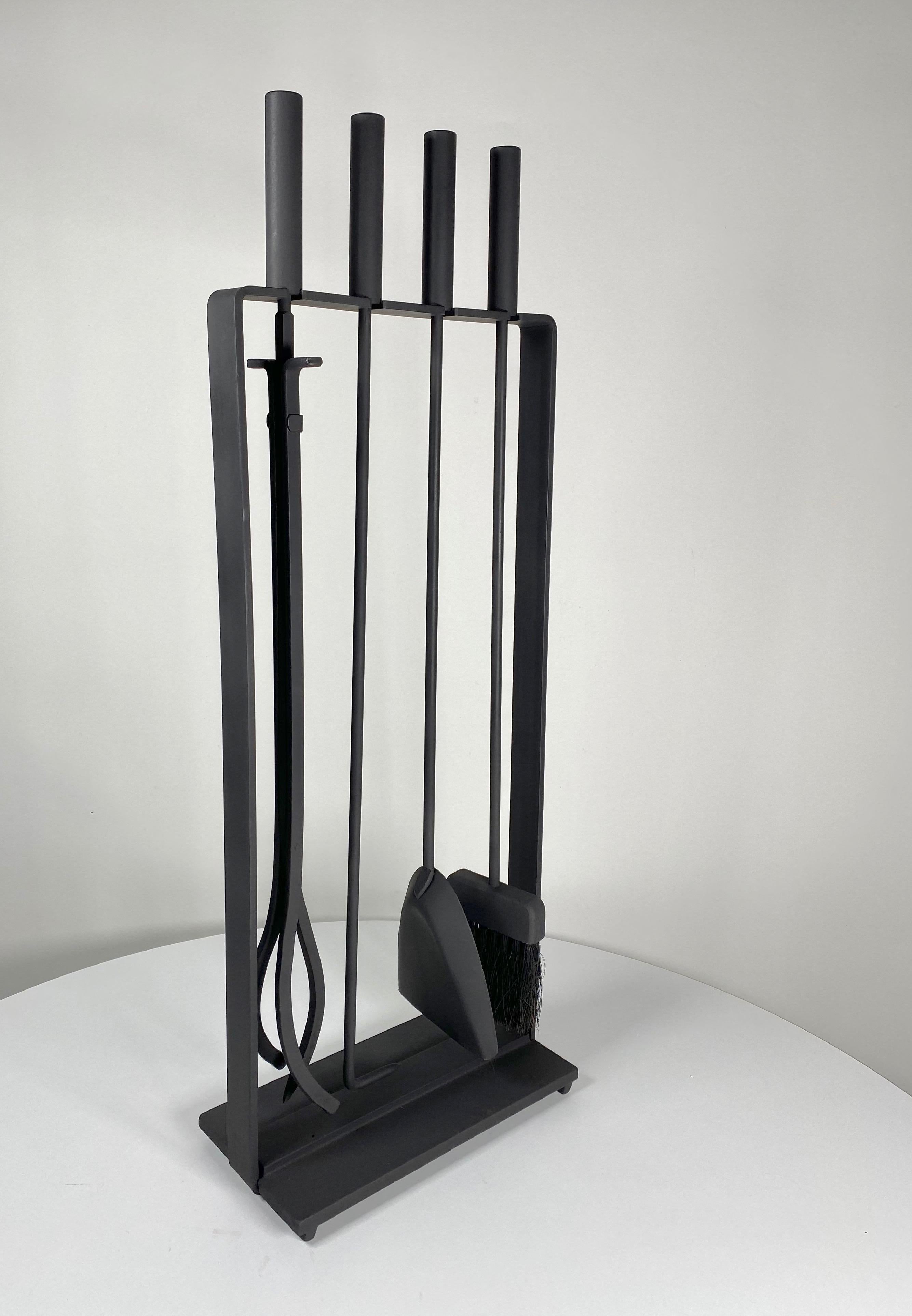 Five piece fireplace tool set, consisting of a dust pan, brush, poker and log grabber with a steel and cast iron frame to hold the tools. Made by Pilgrim Fireplace Tools of the U.S.A. painted in a black matte high temperate paint. Marked on the