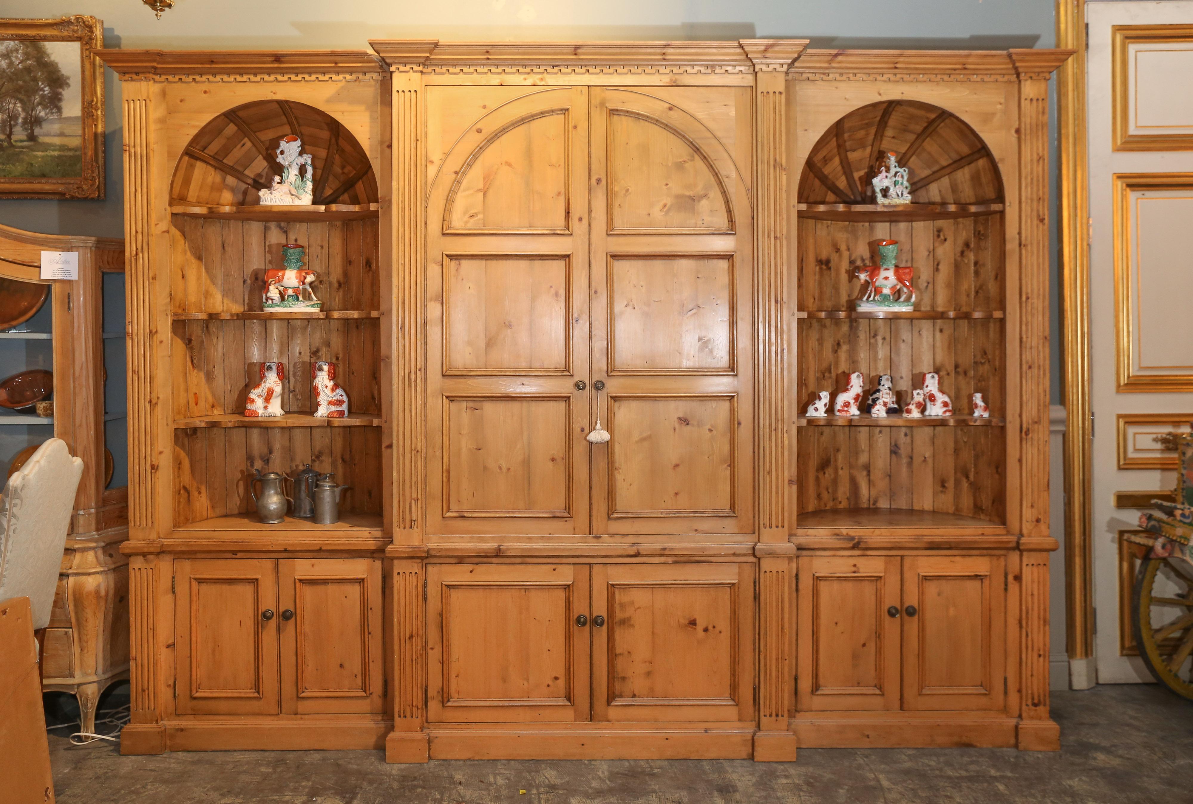 Vintage pine cabinet has closed arched doors for storage and shaped shelving for
display on either side.

