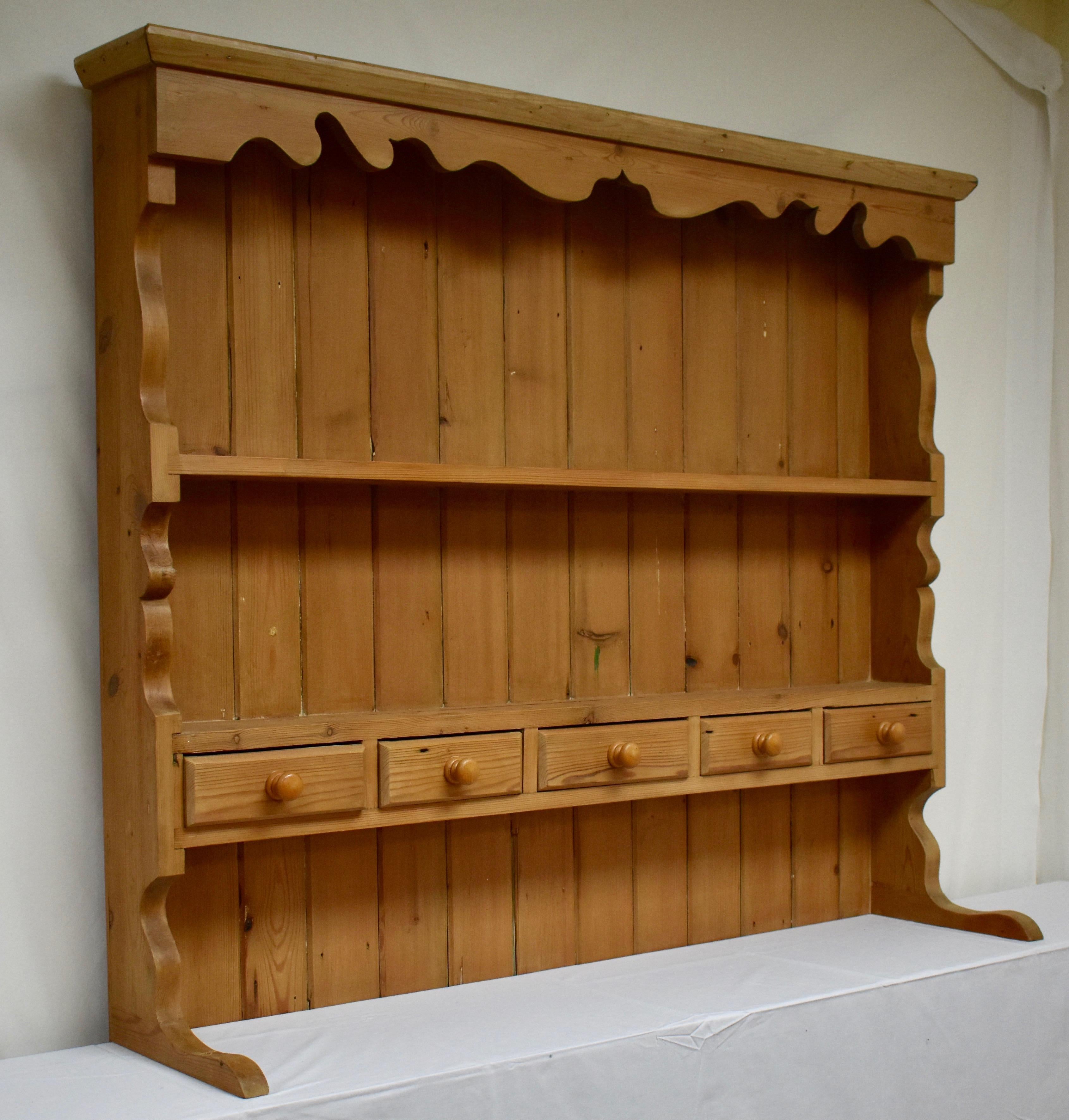 This open rack of shelves, reproduced in old pine in England in the 1970s, has lost its base. Beneath a simple crown molding is a scalloped frieze. The sides, also scalloped, support two shelves, each with a plate groove, and with five lap-jointed