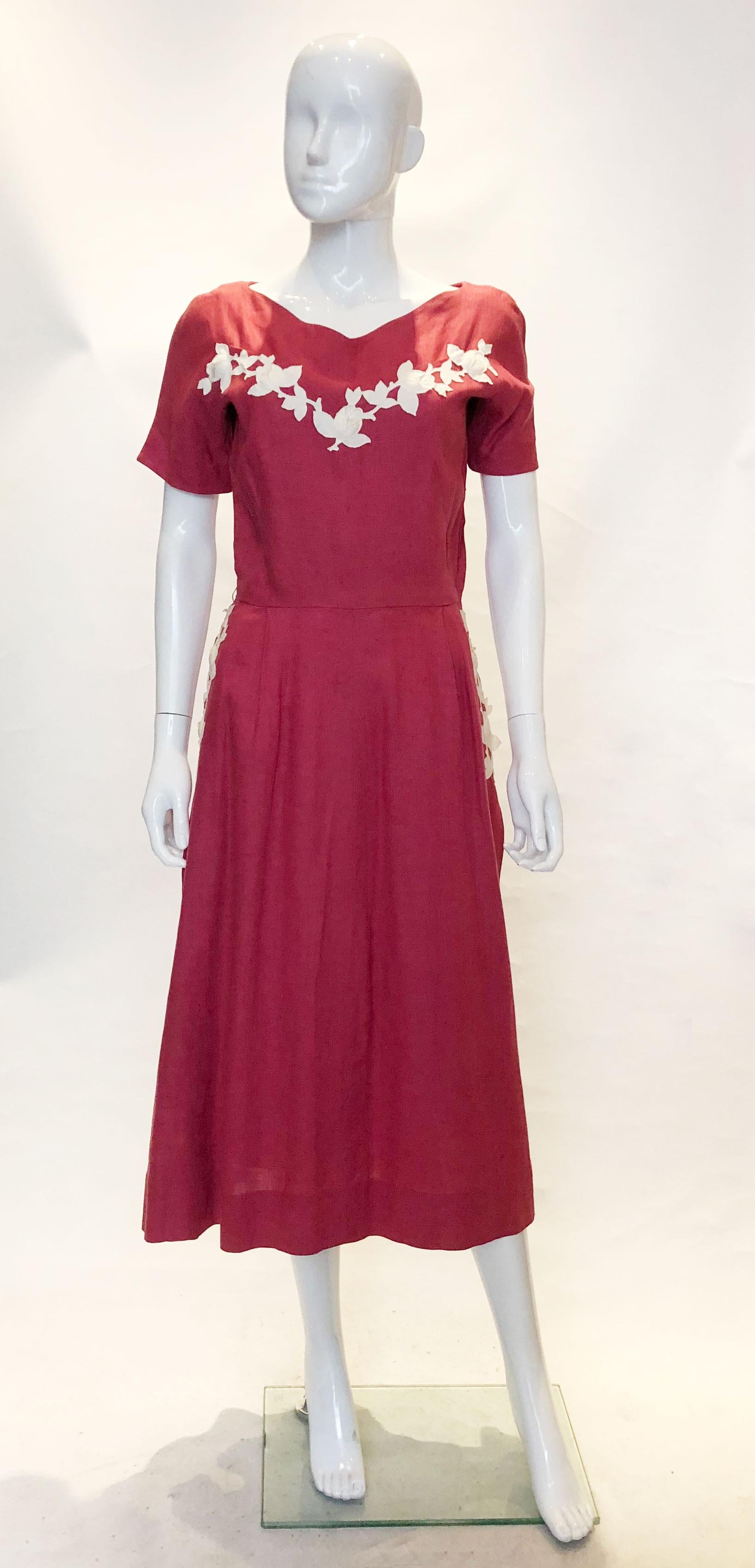 A pretty linen dress from the 1950s. The dress has a v neckline with a row of rosebuds. It has short sleaves , a flared skirt with pockets on either side and a side zip opening. The rose buds are stuffed, giving an extra dimension to the dress.