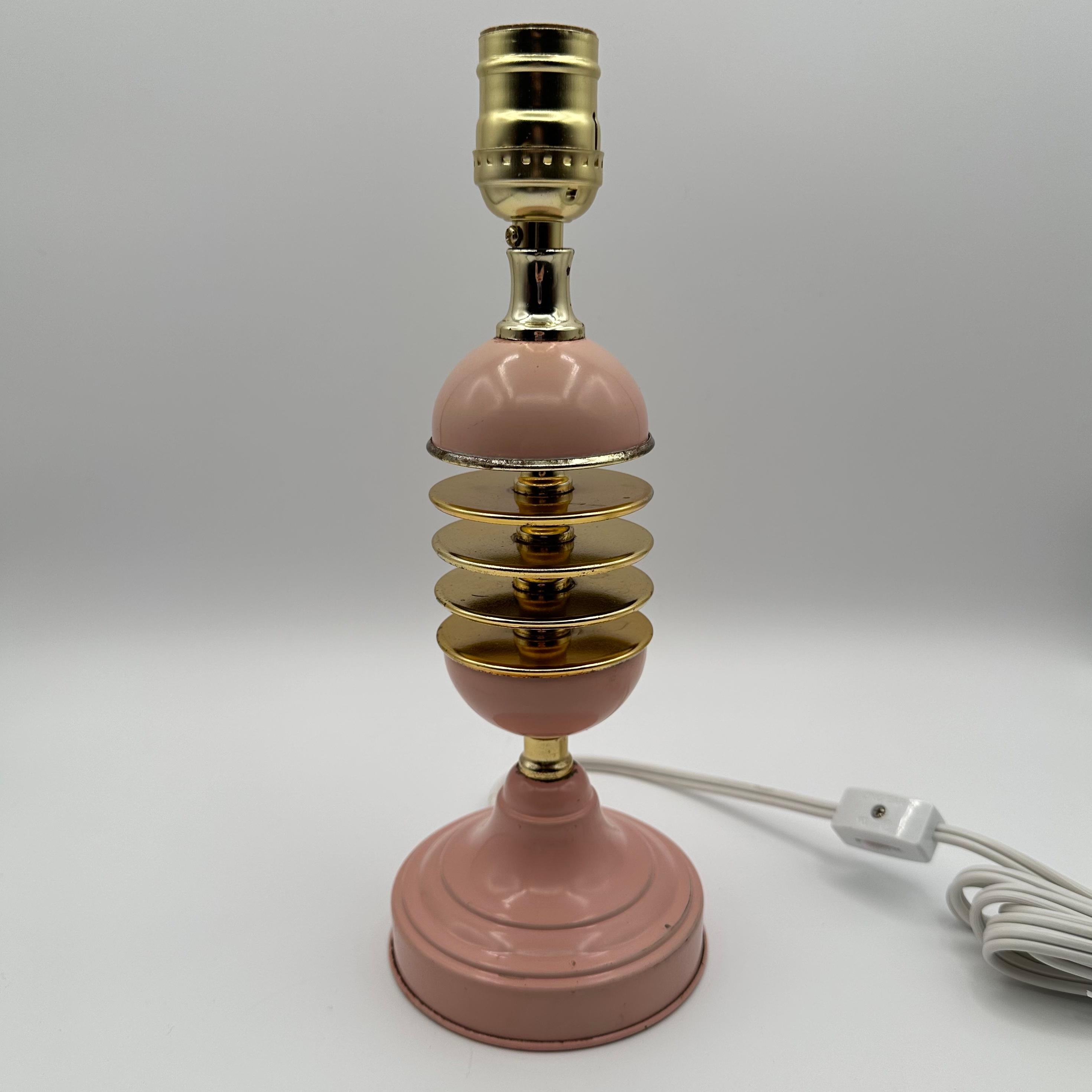 Vintage table lamp in pink and brass with a body comprised of round floating discs suspended in levels between brass pieces. Reminiscent of a hasselback potato, this charming lamp is a charming feminine touch. 

Please review photos carefully; this