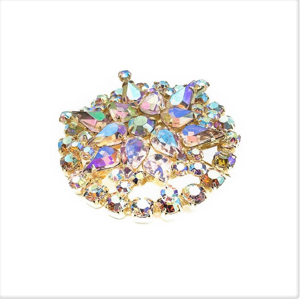 A Vintage Starburst Brooch. Featuring a myriad of fancy cut, claw set, lilac pink auorora borealis crystals in a starburst style with an outer circle to finish. Crafted in glass and gold tone metal. In very good vintage condition. 5 cms. A fabulous