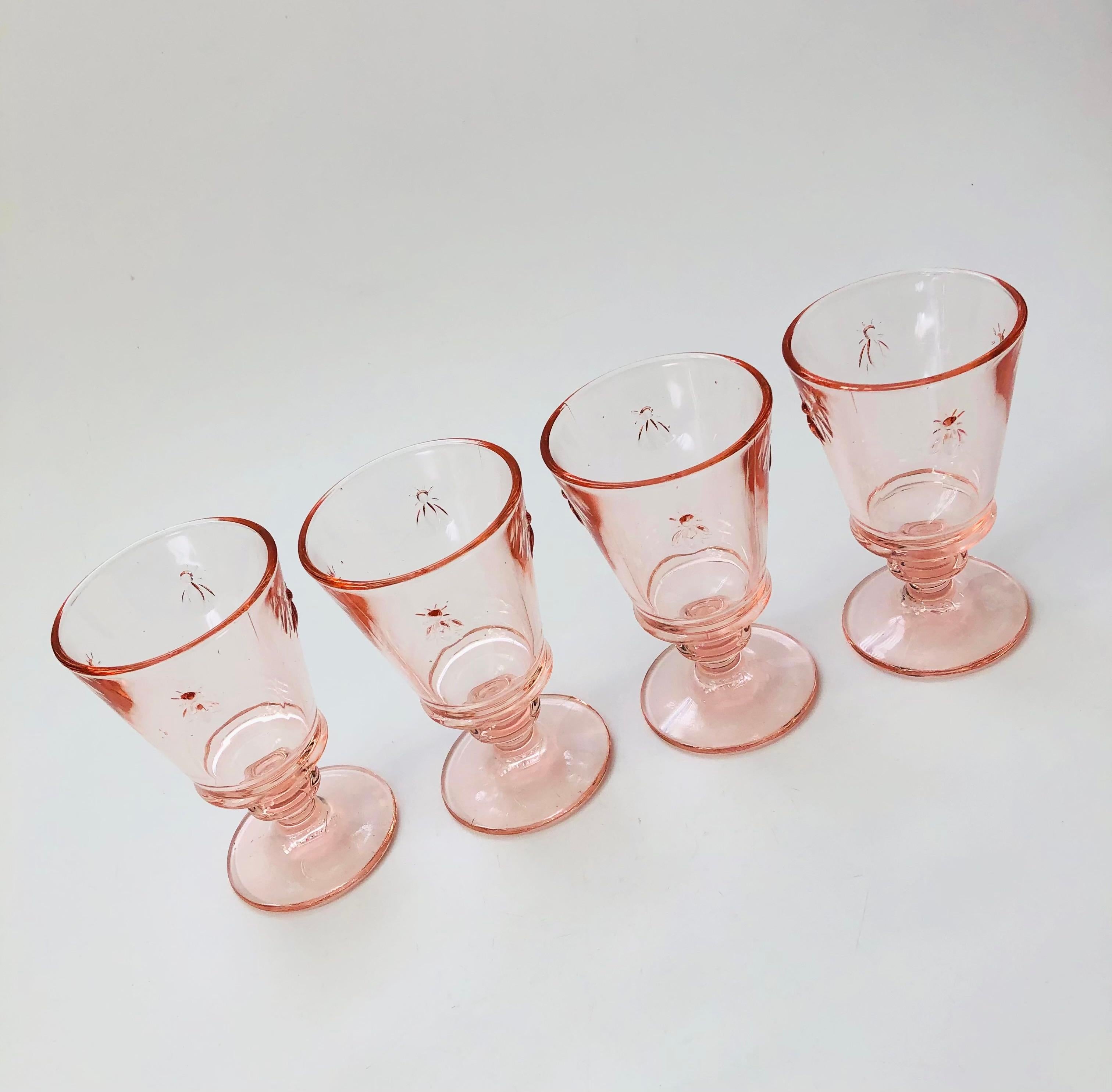 A set of 4 vintage wine glasses in a pale blush pink hue. Each glass is decorated with embossed Napoleonic bees around the sides. Made in France by La Rochere.

