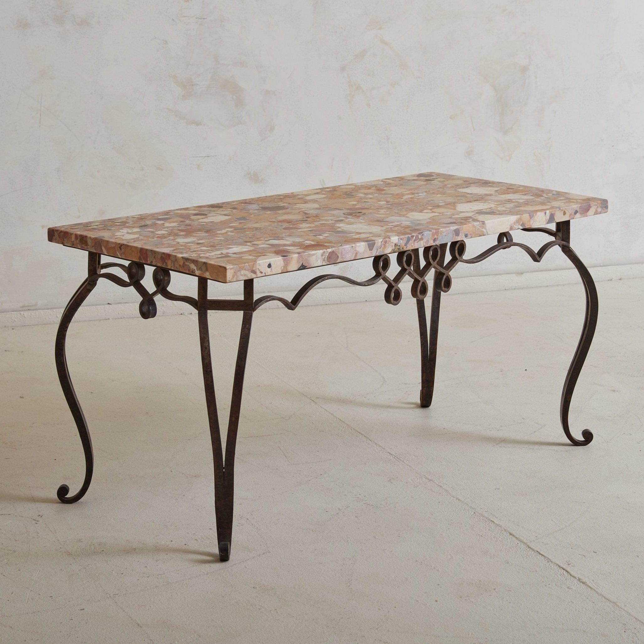A gorgeous honed pink marble and hand forged iron base coffee table sourced in Italy. Varying hues of orange, lavender, and red can be seen throughout the intricately veined marble top. The ornate iron frame features four curved legs, swirl feet,