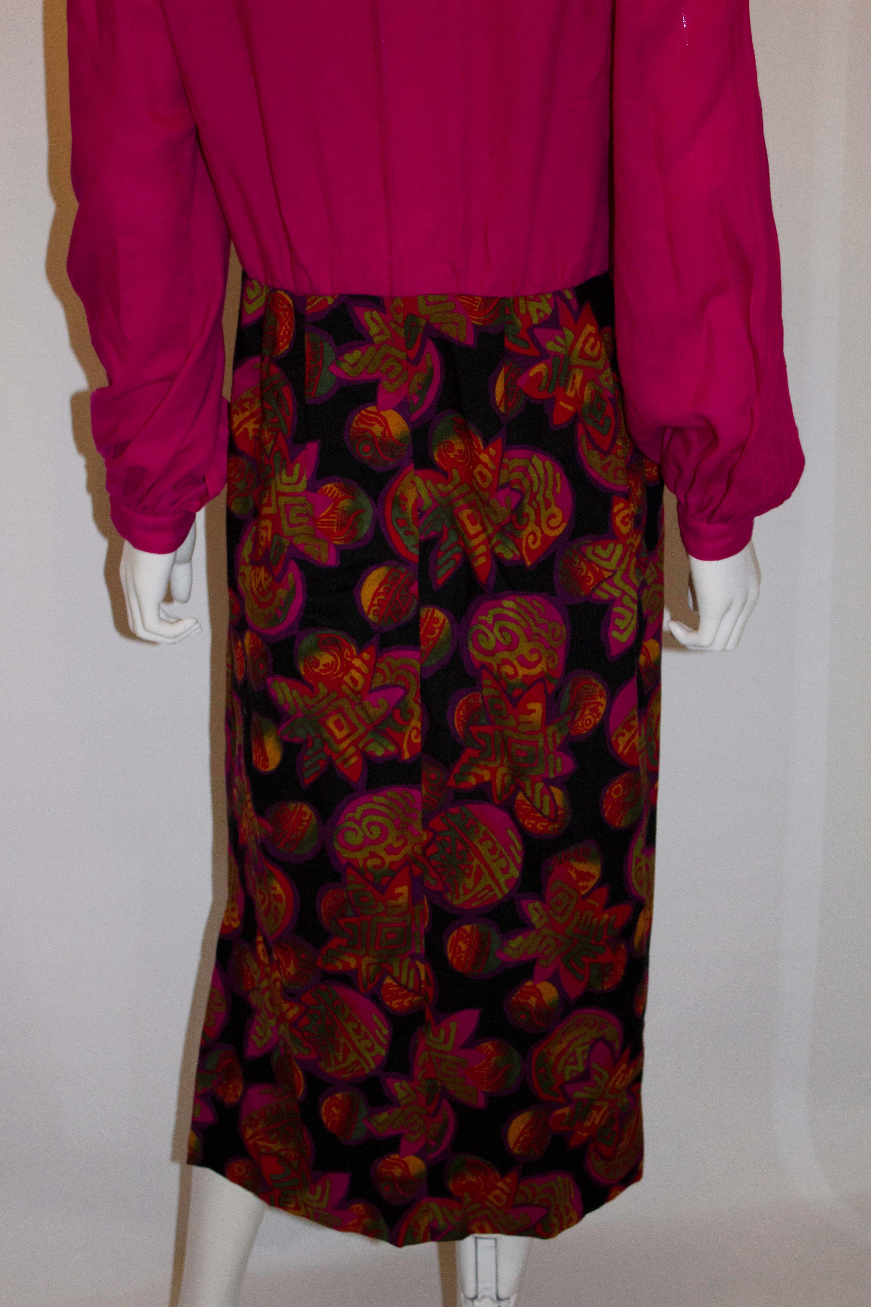 Une jolie robe vintage en crêpe de laine de Donald Campbell. La robe a une partie supérieure rose avec des plis sur le devant et les manches. La zone de la jupe est dans un imprimé. La robe a une fermeture éclair centrale au dos et est doublée.