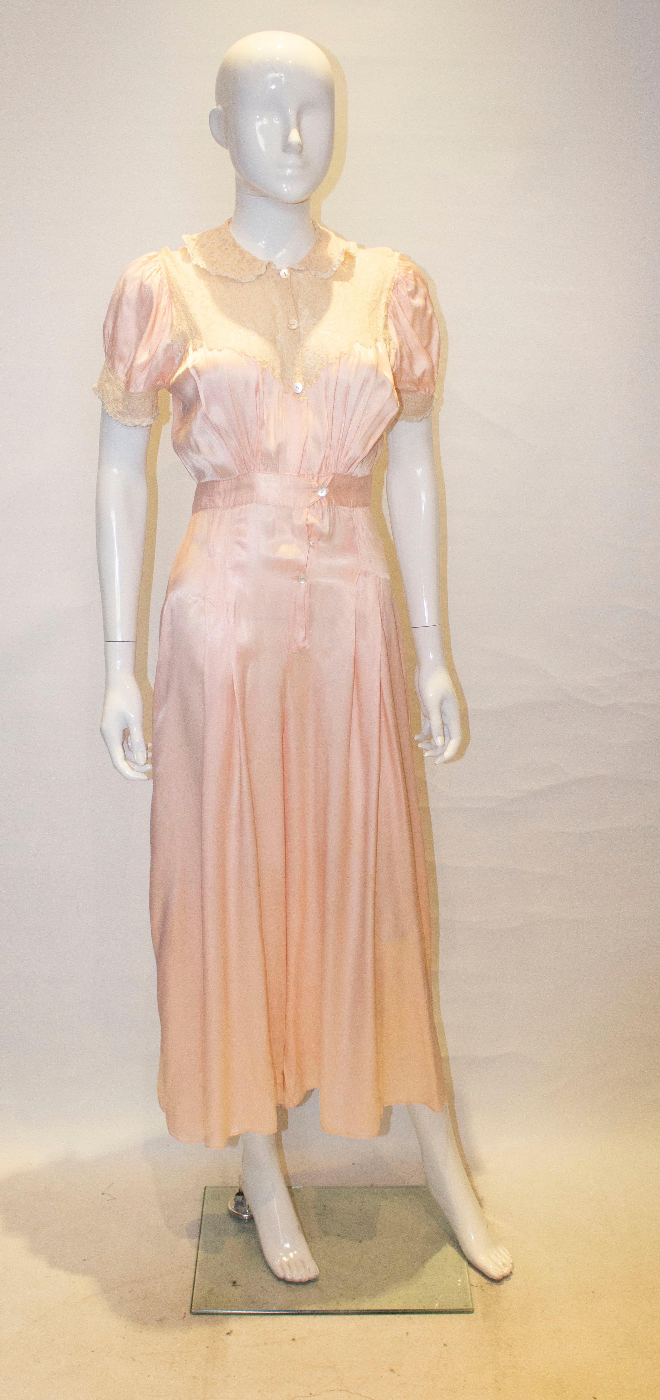 A stylish and unusual jumpsuit.  In a pretty pink satin, it has a lace collar and trim on the bodice and cuffs. It has a five button front opening with gathering at waist leval front and back, and pleats and hip leval front and back. 
Measurements: