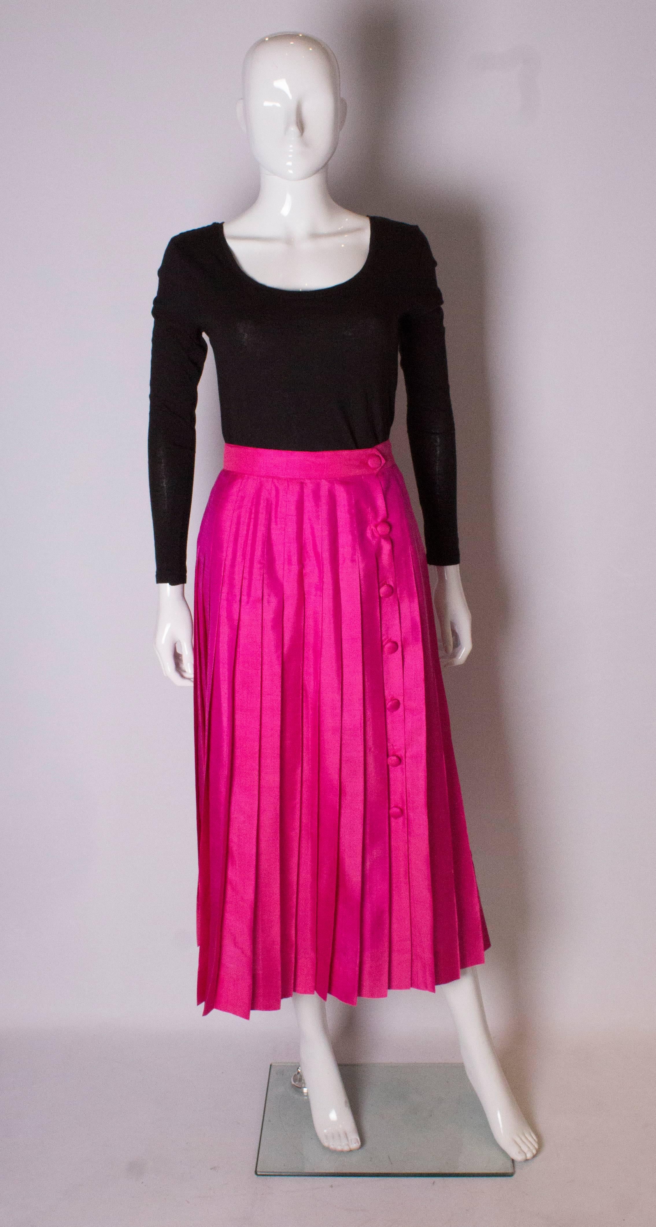 A chic pink silk skirt. The silk skirt has sewn down pleats from the waist band, producing a smooth line . It has a button opening on the right hand side, and the buttons are covered in the same pink silk.