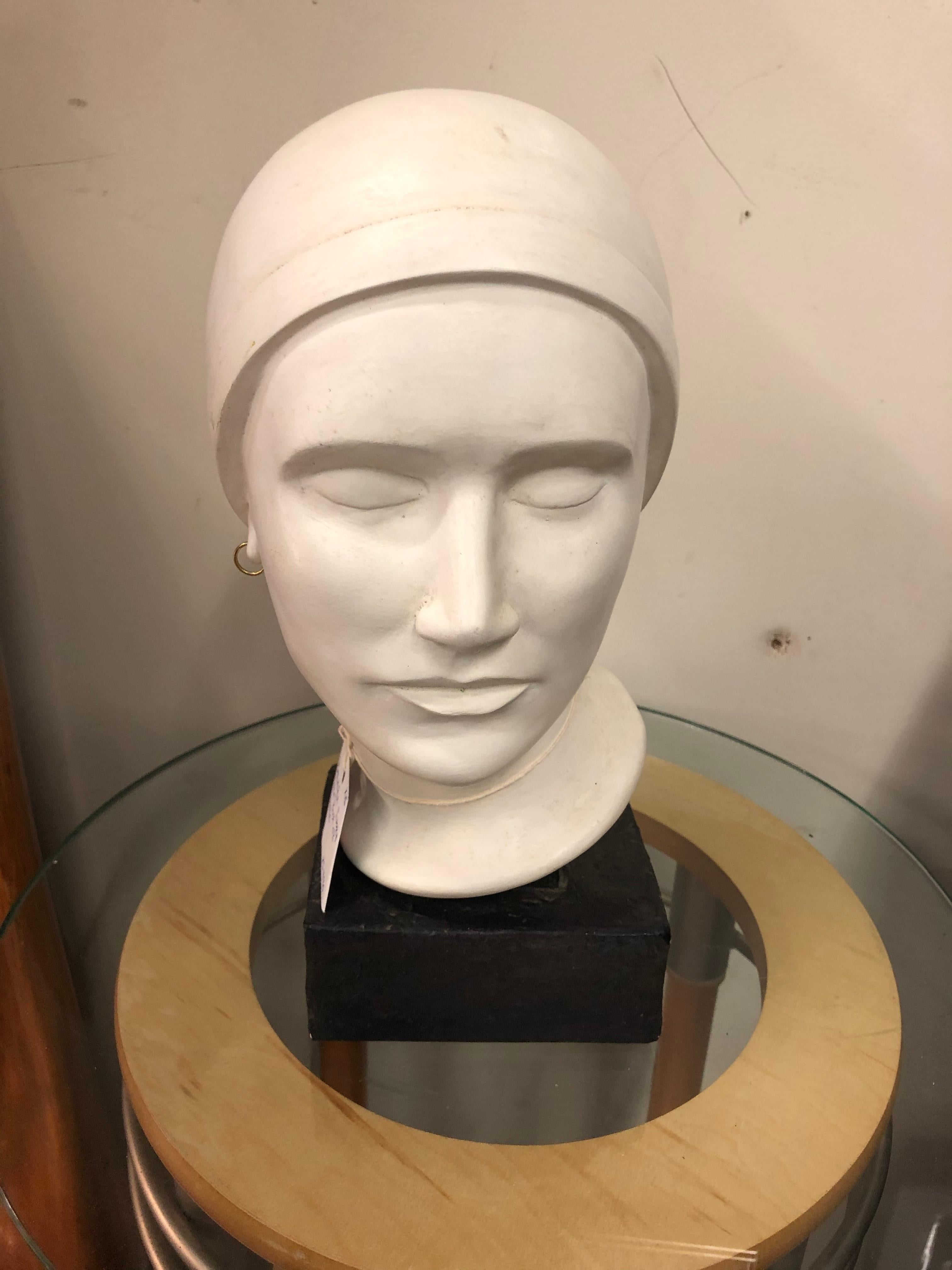 A beautiful plaster bust of a woman mounted on a plaster base. Made in the Art Deco style, the woman is wearing a close fitting hat and one earring; her eyes are cast downwards. The bust has a felt bottom which is signed 